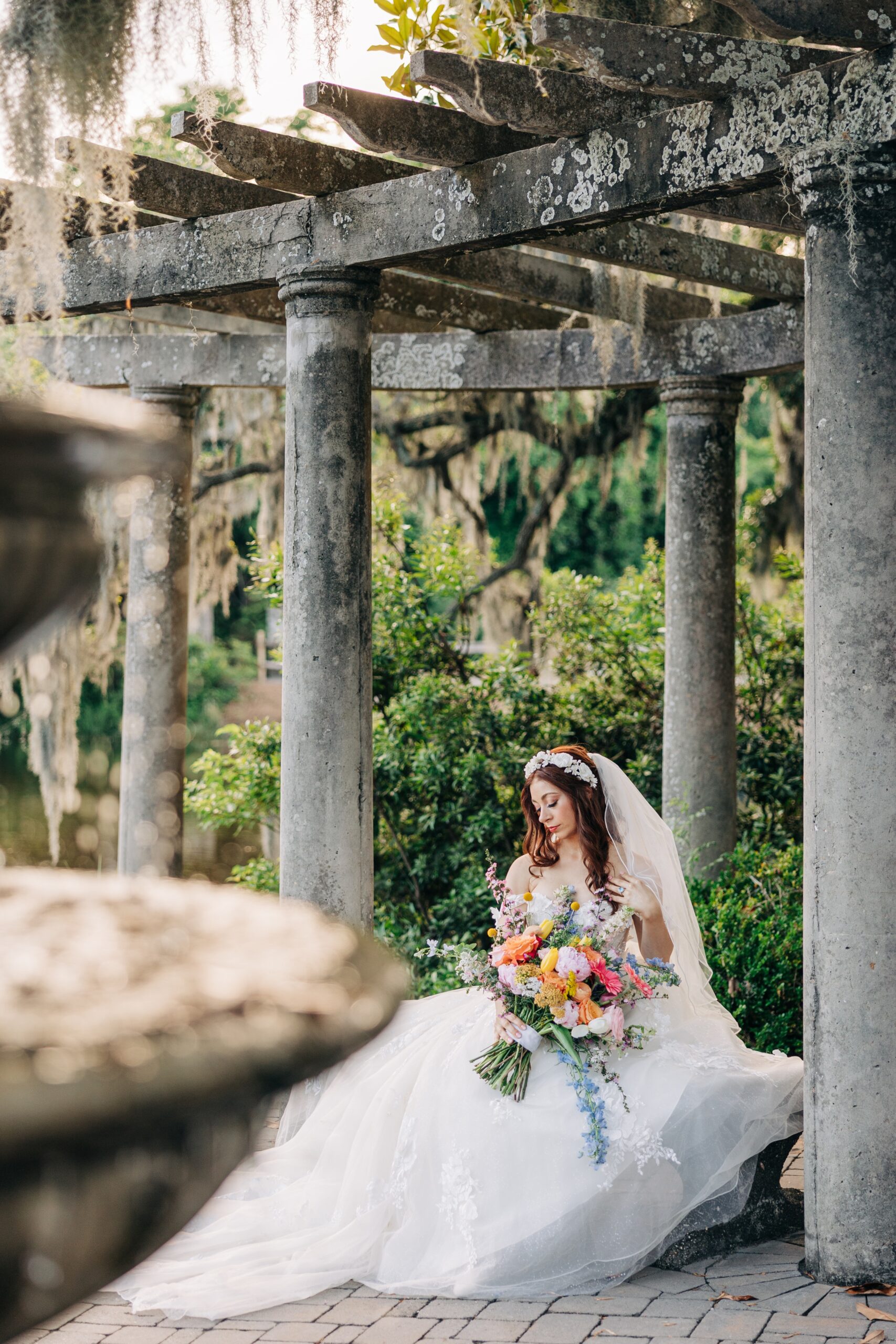 A bride gazes down her shoulder while sitting on a gazebo bench before her Airlie Gardens wedding