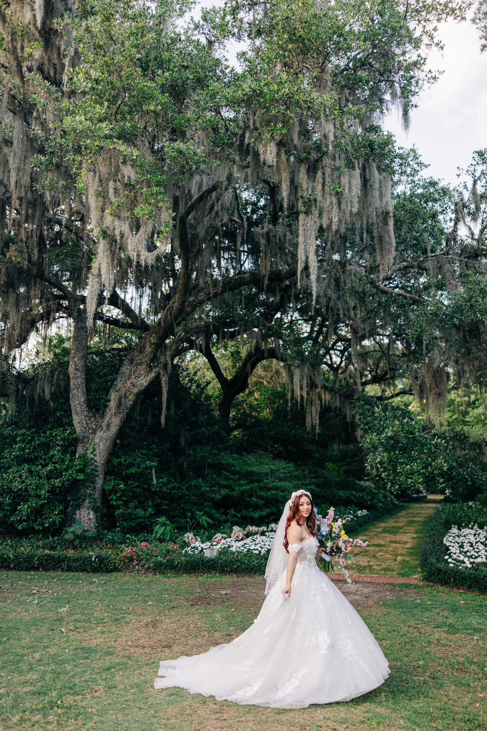 A bride walks through a lawn holding her train and bouquet to her Airlie Gardens wedding