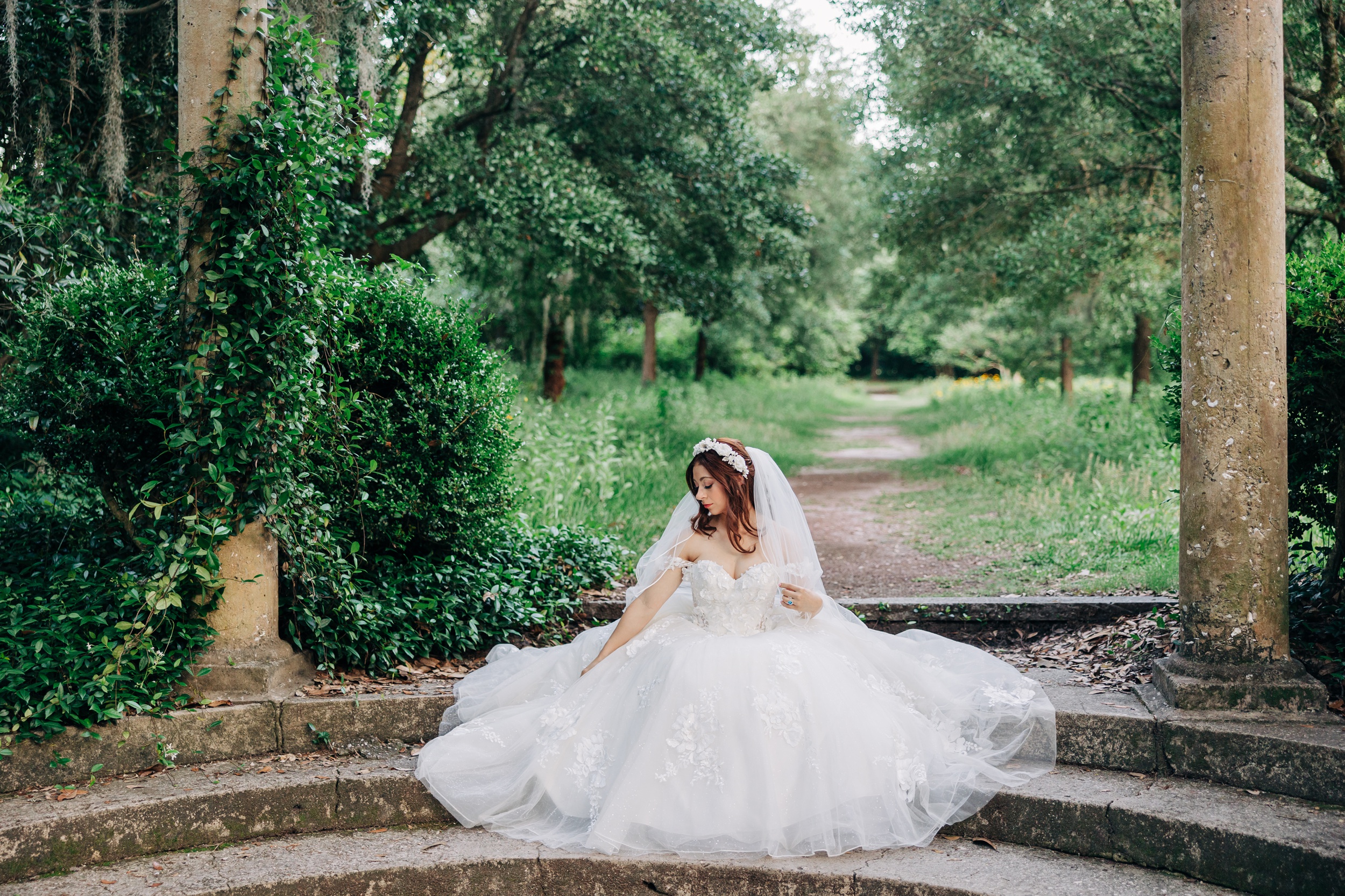 A bride sits on garden steps looking down her shoulder during her Airlie Gardens wedding