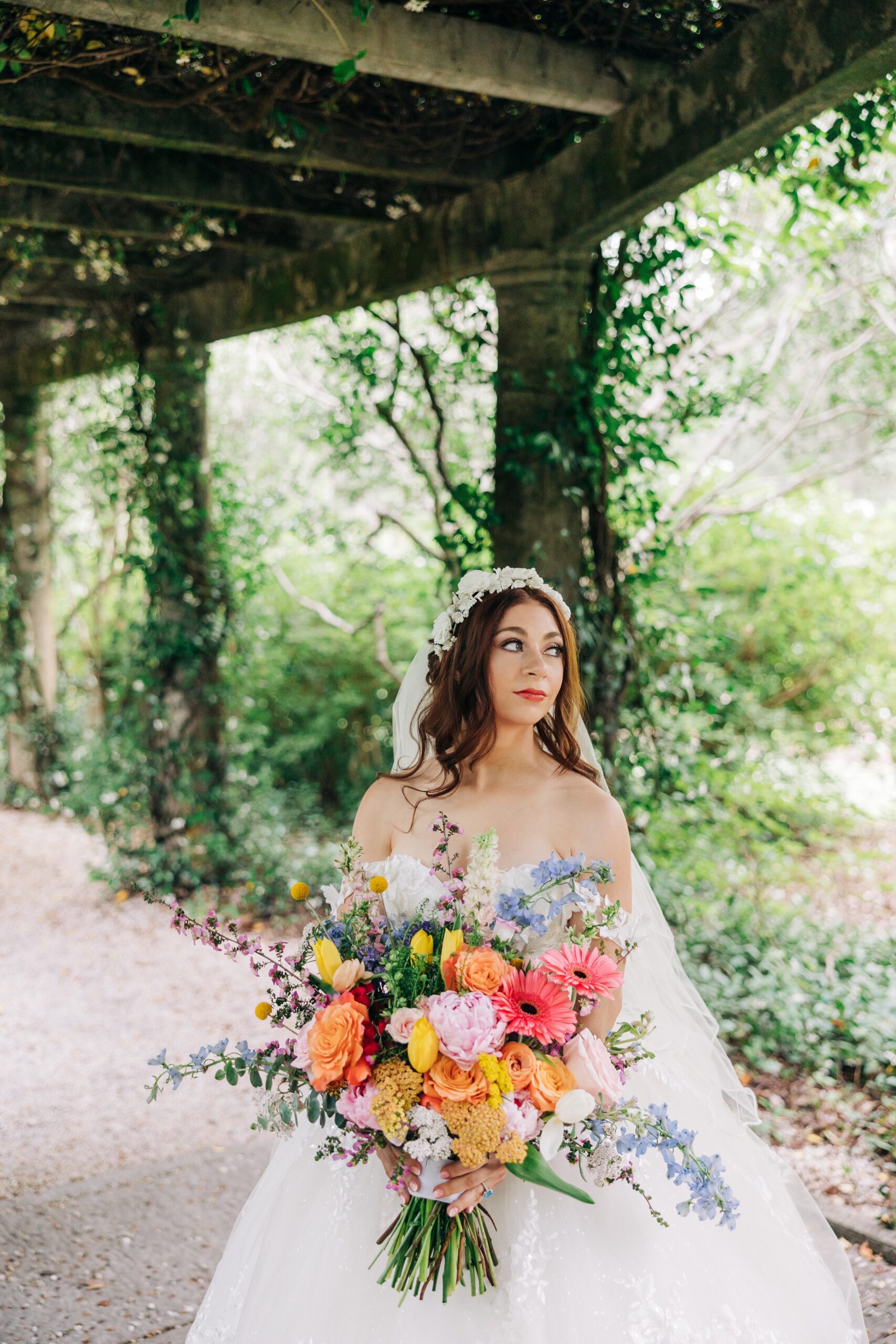 A bride smiles over her shoulder to a garden while holding her bouquet