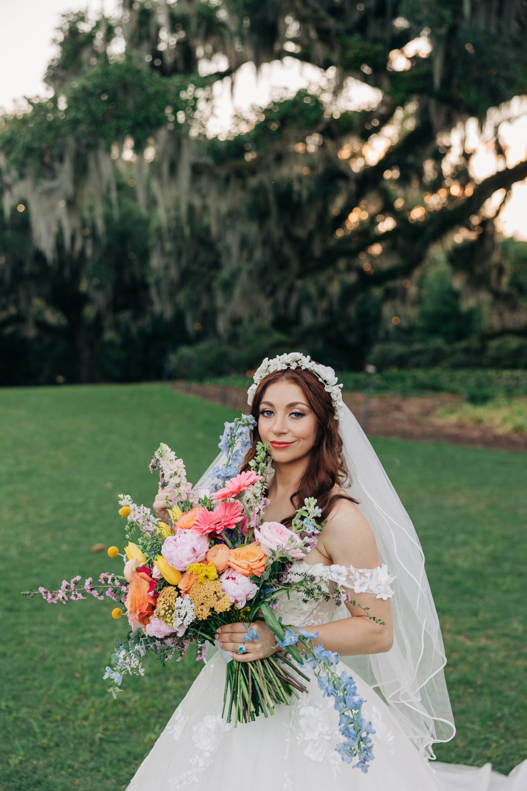 A bride smiles while holding her colorful bouquet in a lawn at sunset