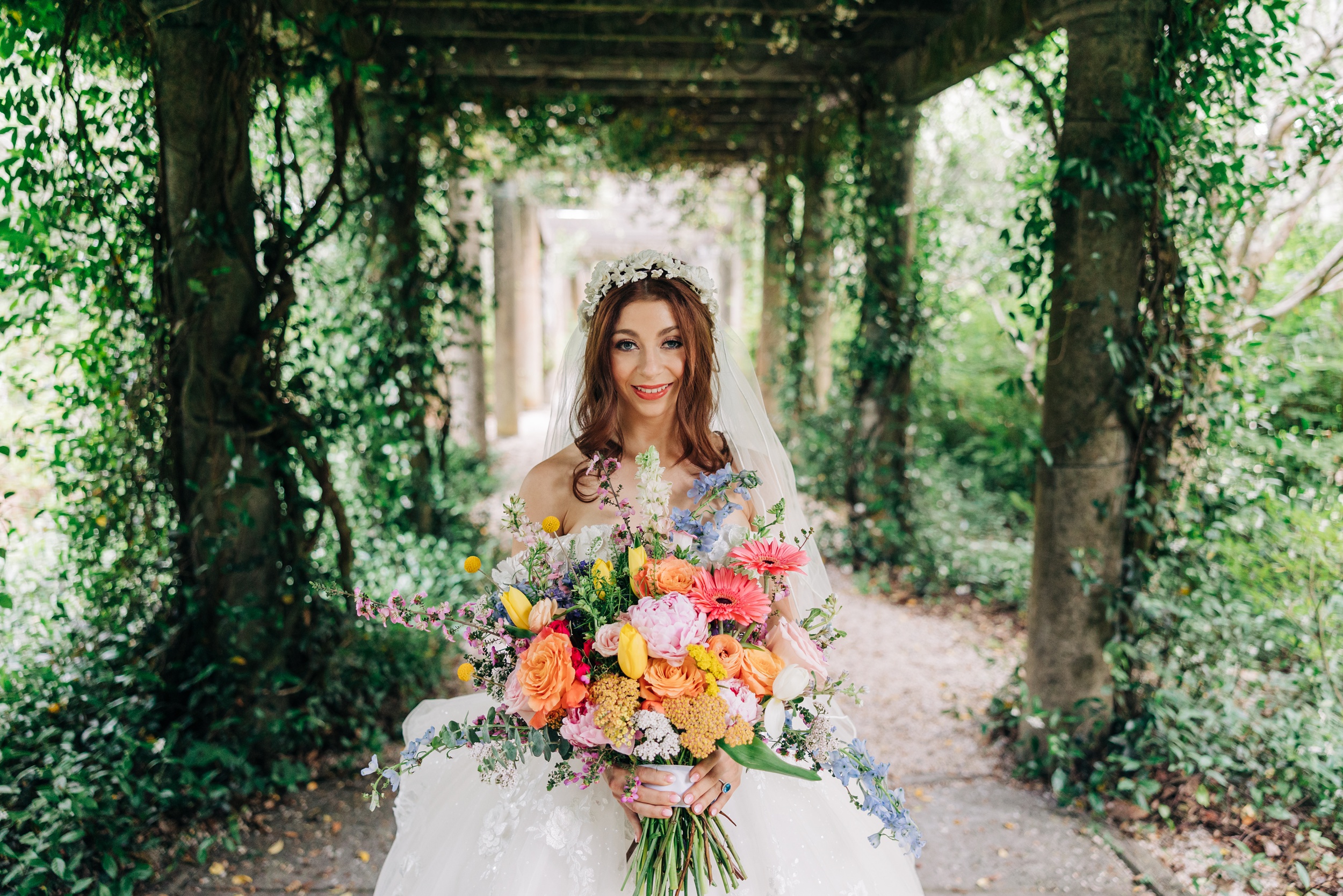 A happy bride walks in a covered walkway holding a large bouquet full of color