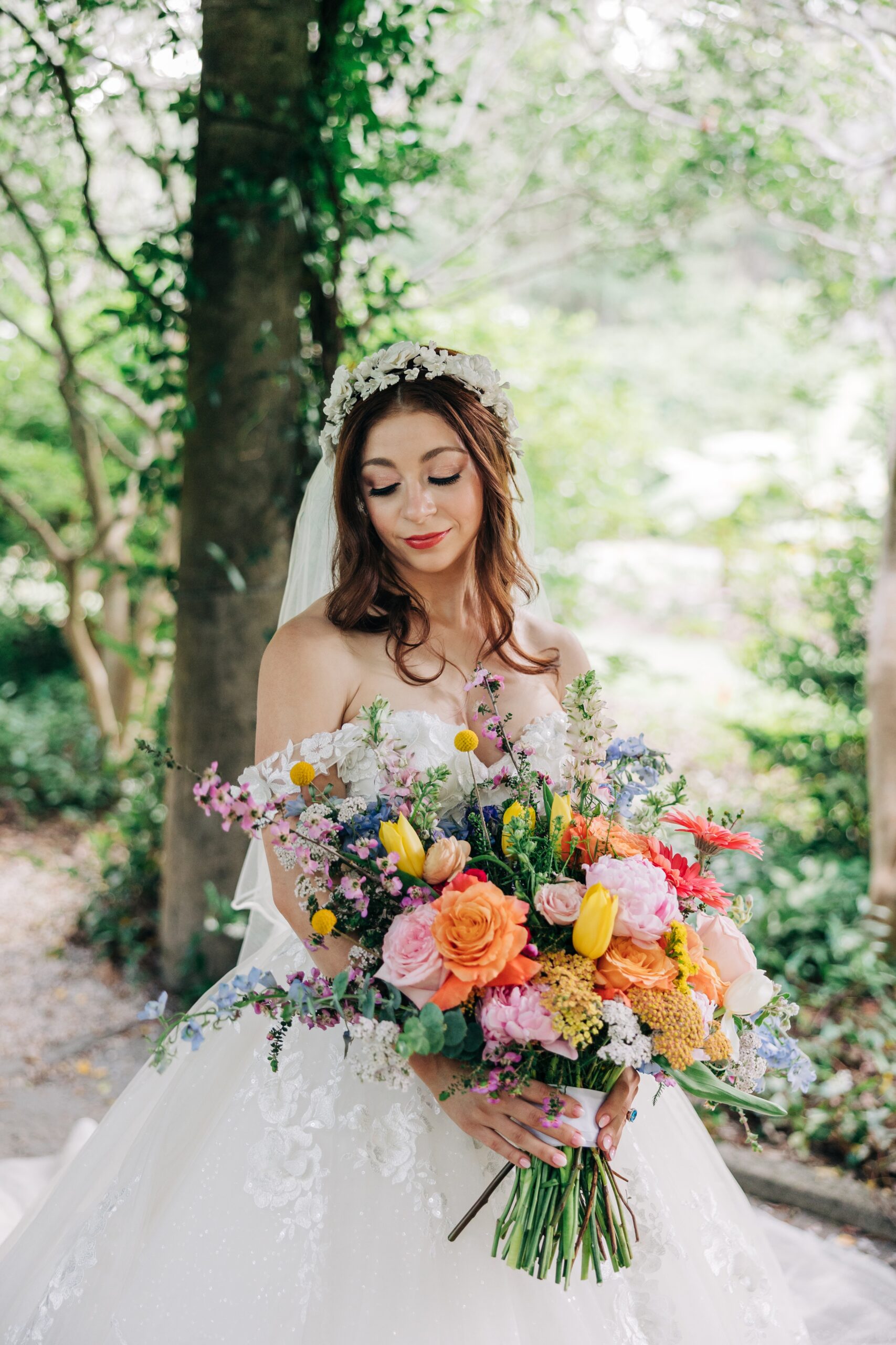 A bride smiles down to her large vibrant bouquet in front of her while walking in a garden