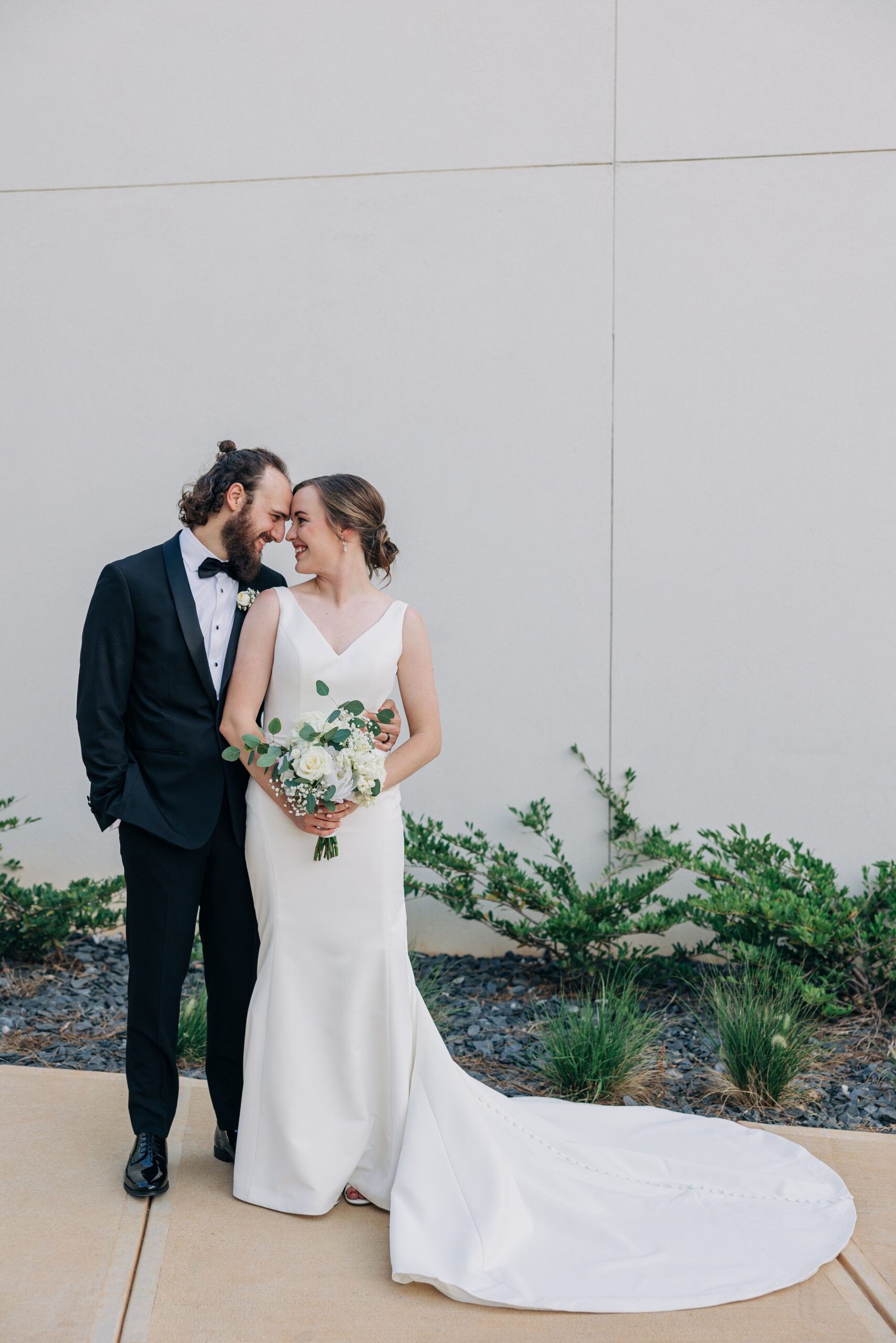 Newlyweds smile while touching foreheads and standing in a garden at the pine wedding venue