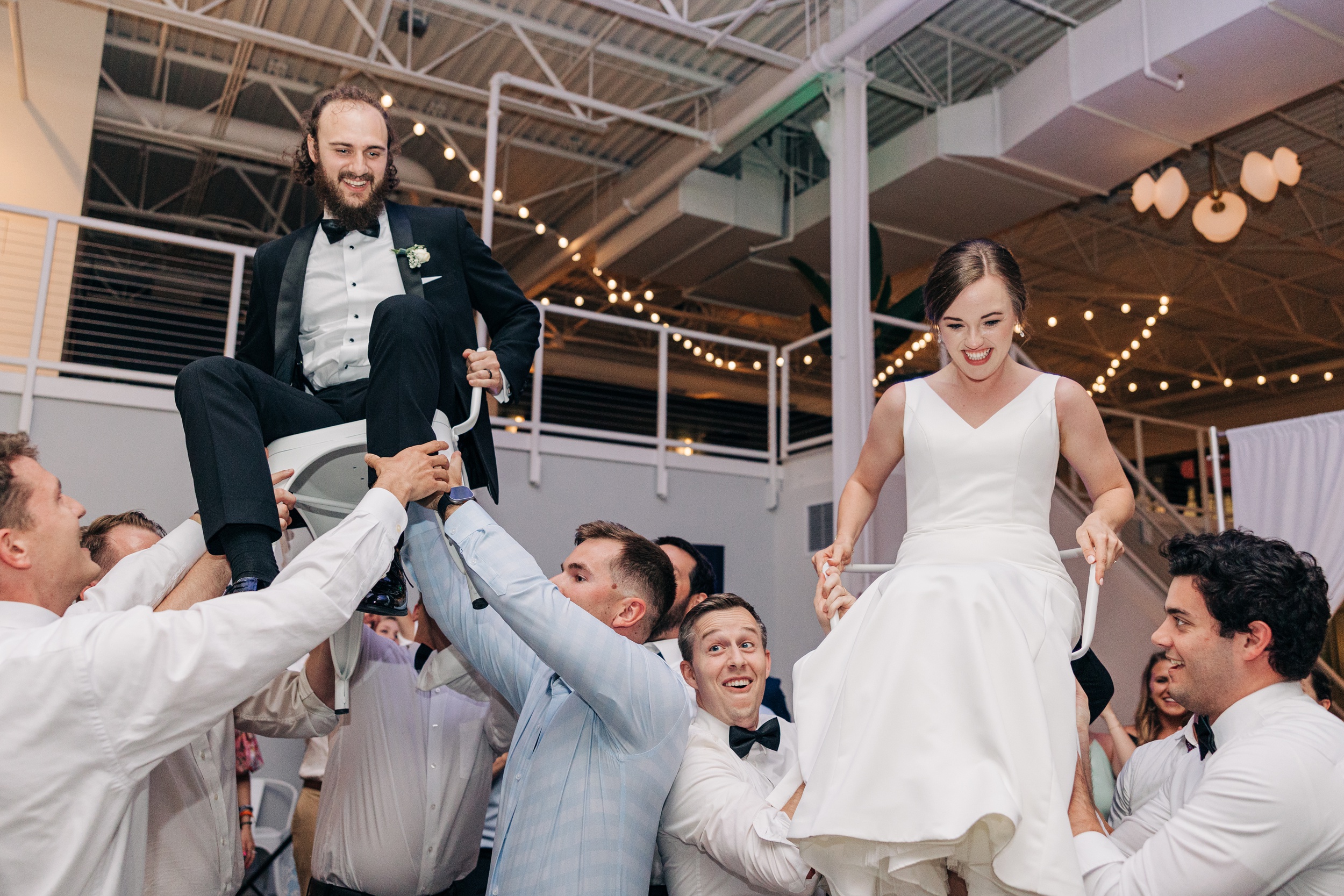 A bride and groom are lifted in chairs on the dance floor