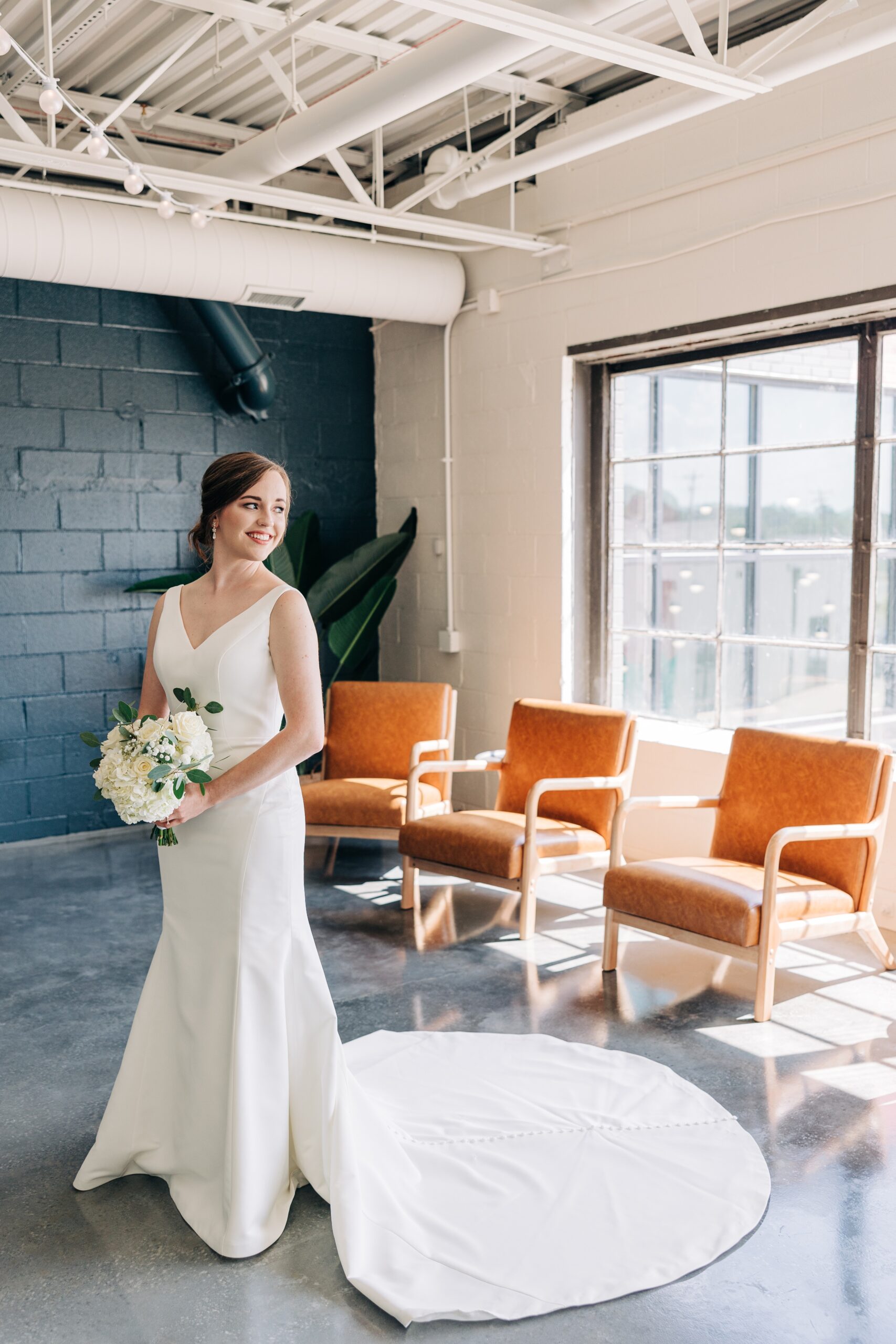 A bride smiles over her shoulder while showing off her dress and bouquet