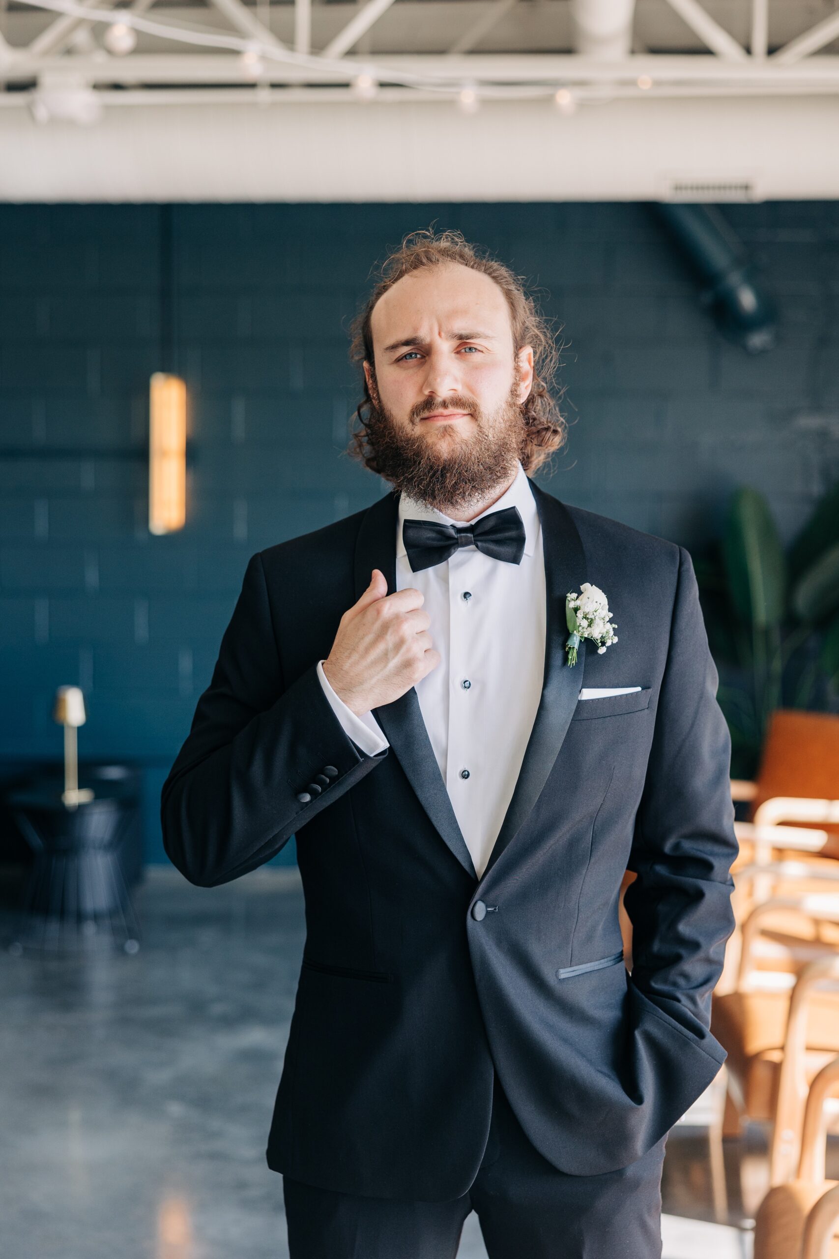 A groom stands in a window holding his lapel