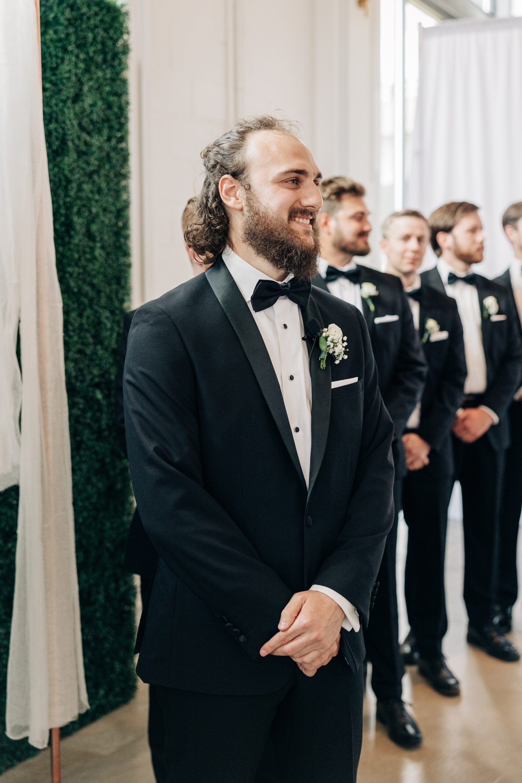 A groom smiles big while waiting for his bride at the altar