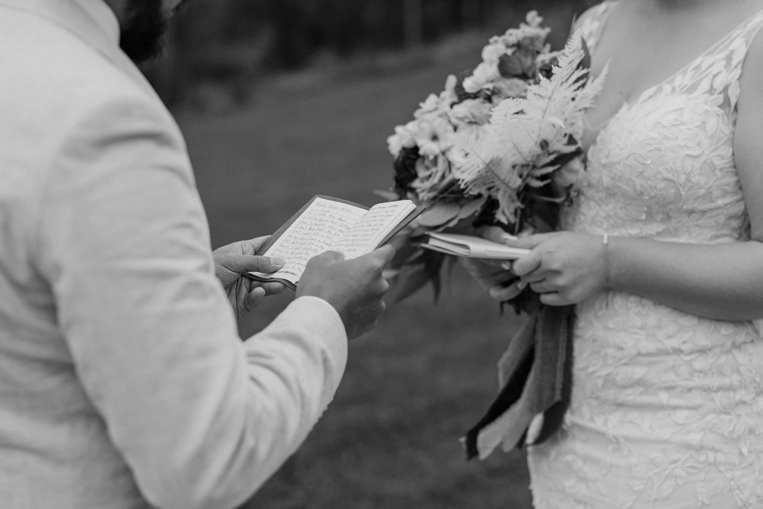 Details of a groom reading a note from a small notebook to his bride