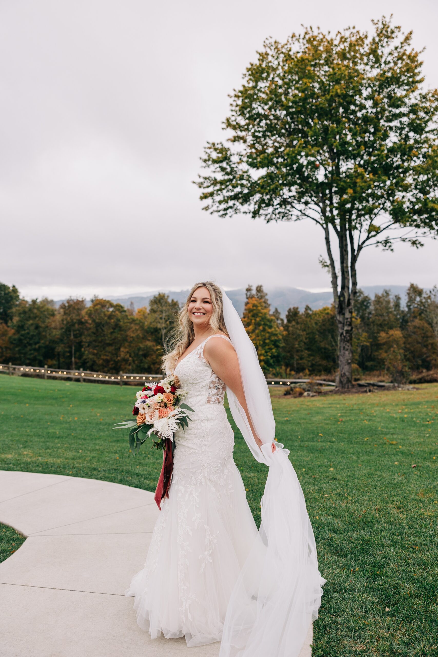 A bride smiles big while holding her colorful bouquet during her appalachian view wedding