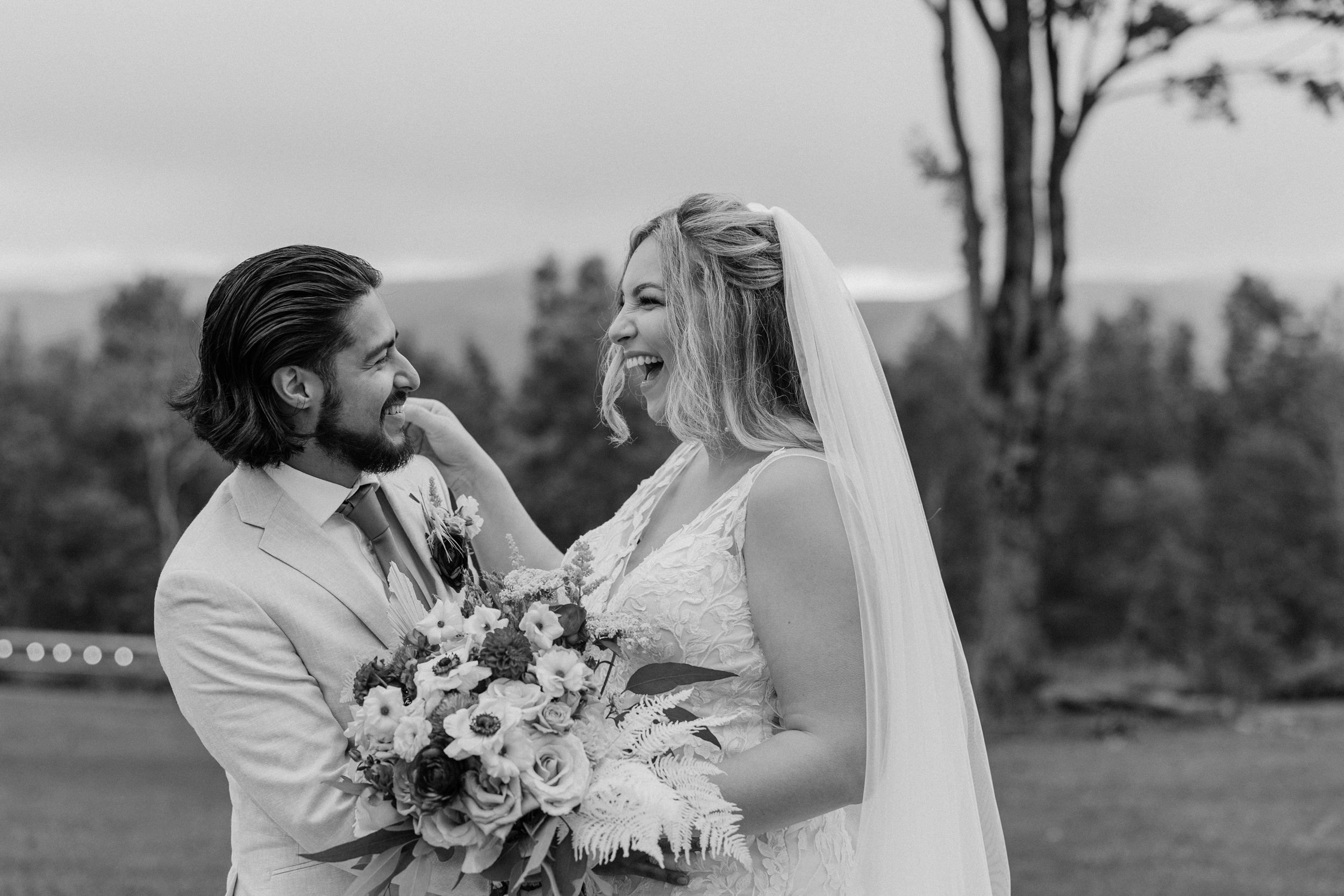 Newlyweds laugh big while hugging in the lawn in black and white