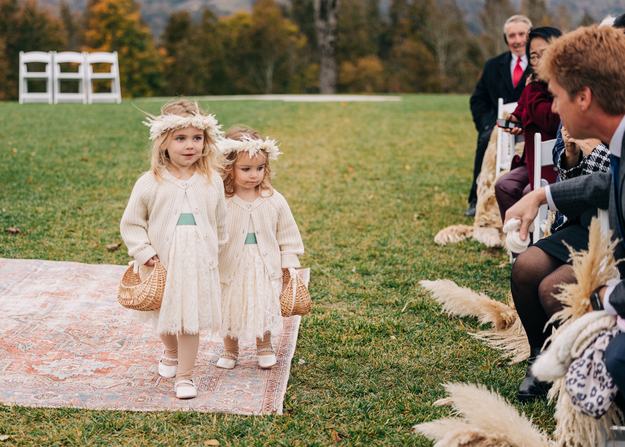 Two toddler girls in matching dresses and headbands spread flowers during an outdoor wedding ceremony