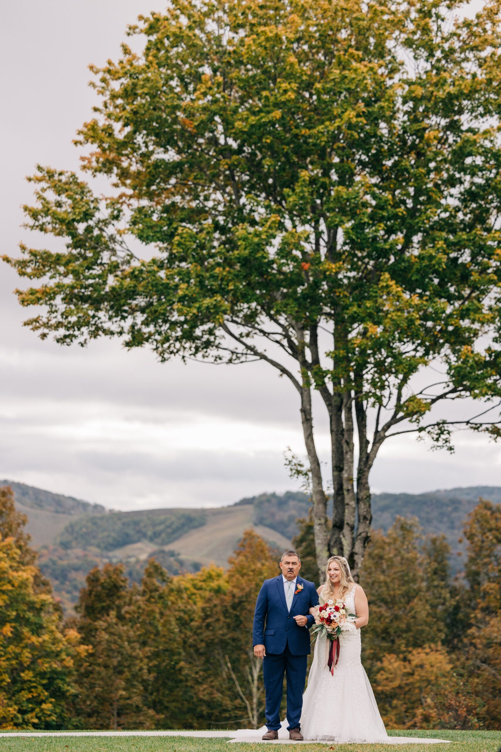 A bride smiles big while walking down the aisle with dad during her appalachian view wedding ceremony