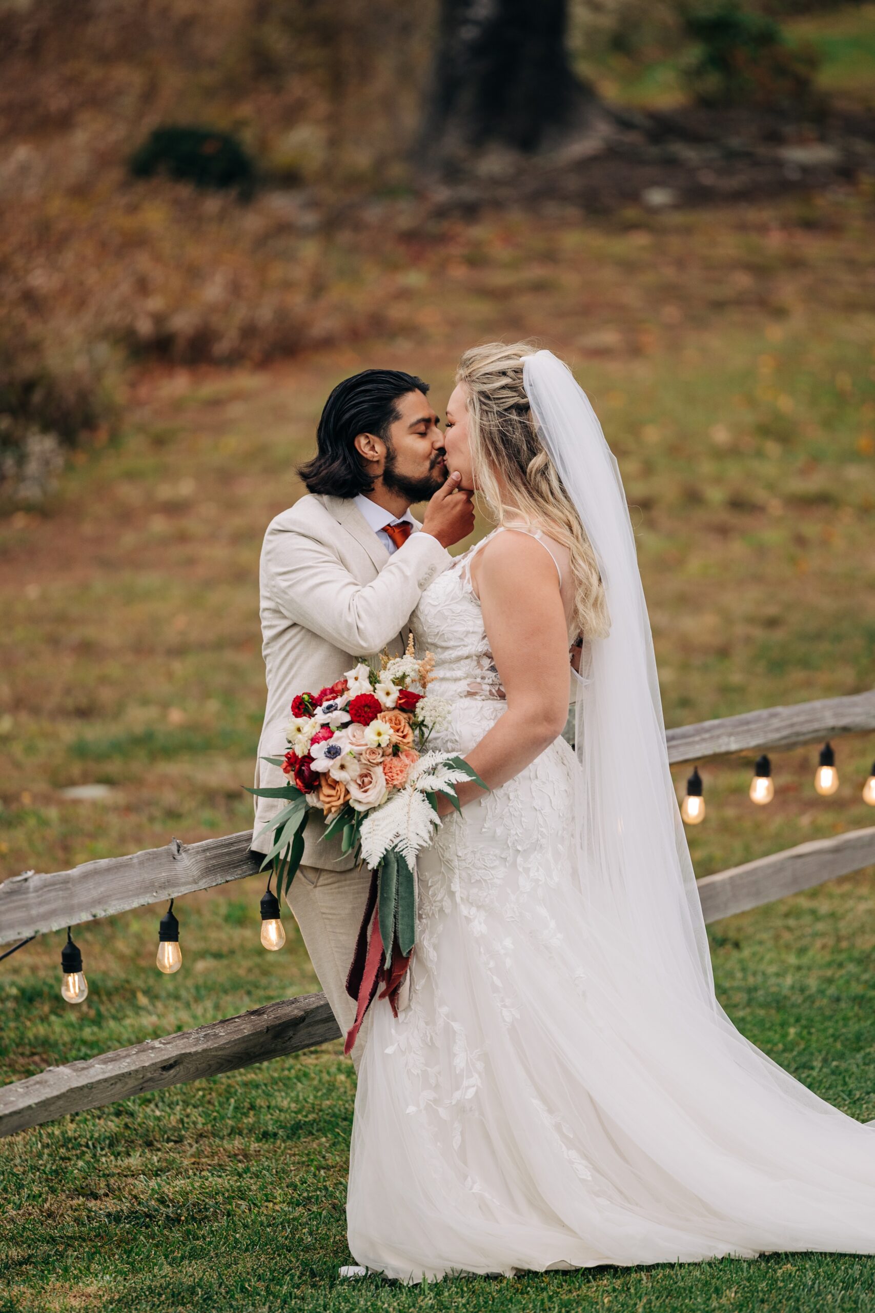 Newlyweds kiss while leaning against a farm fence in the forest during their appalachian view wedding