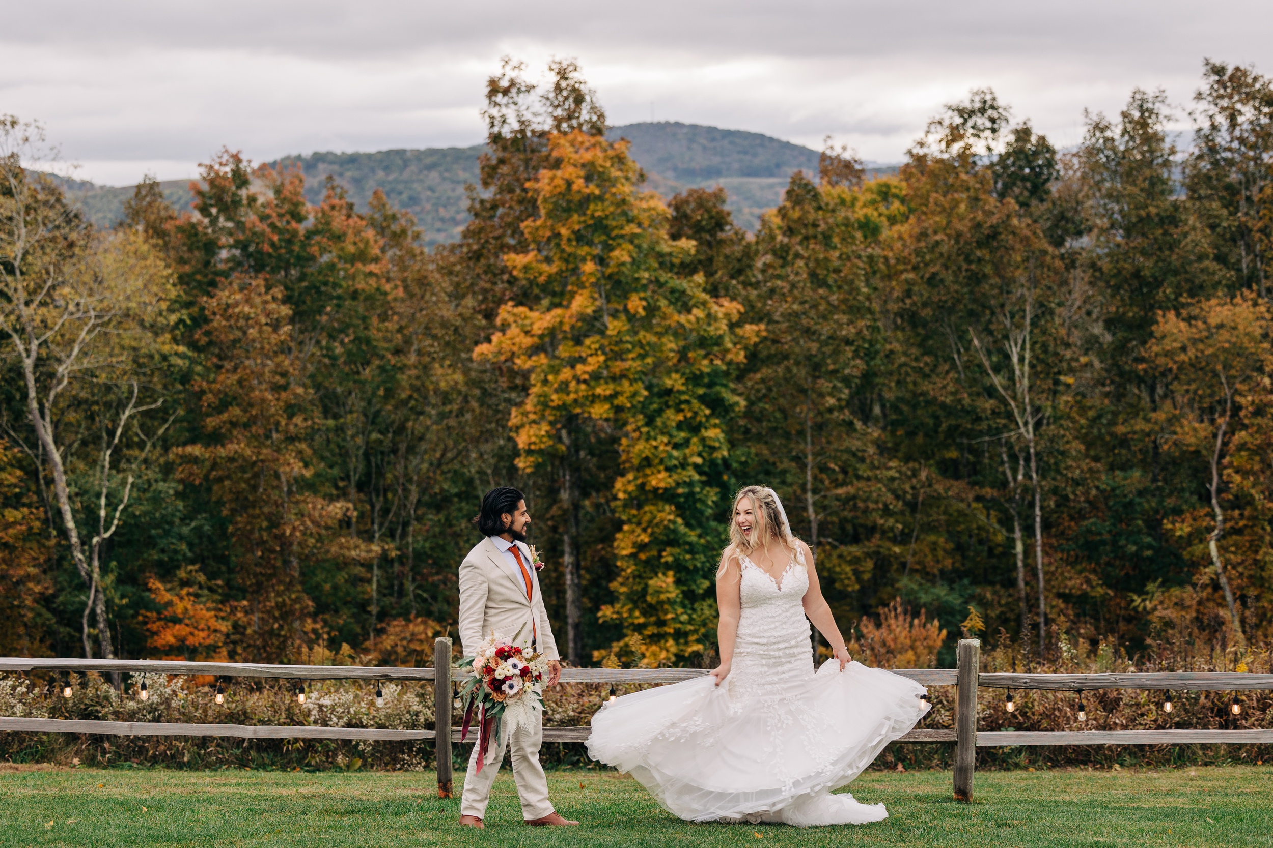 Newlyweds laugh and walk along a wooden farm fence during their appalachian view wedding