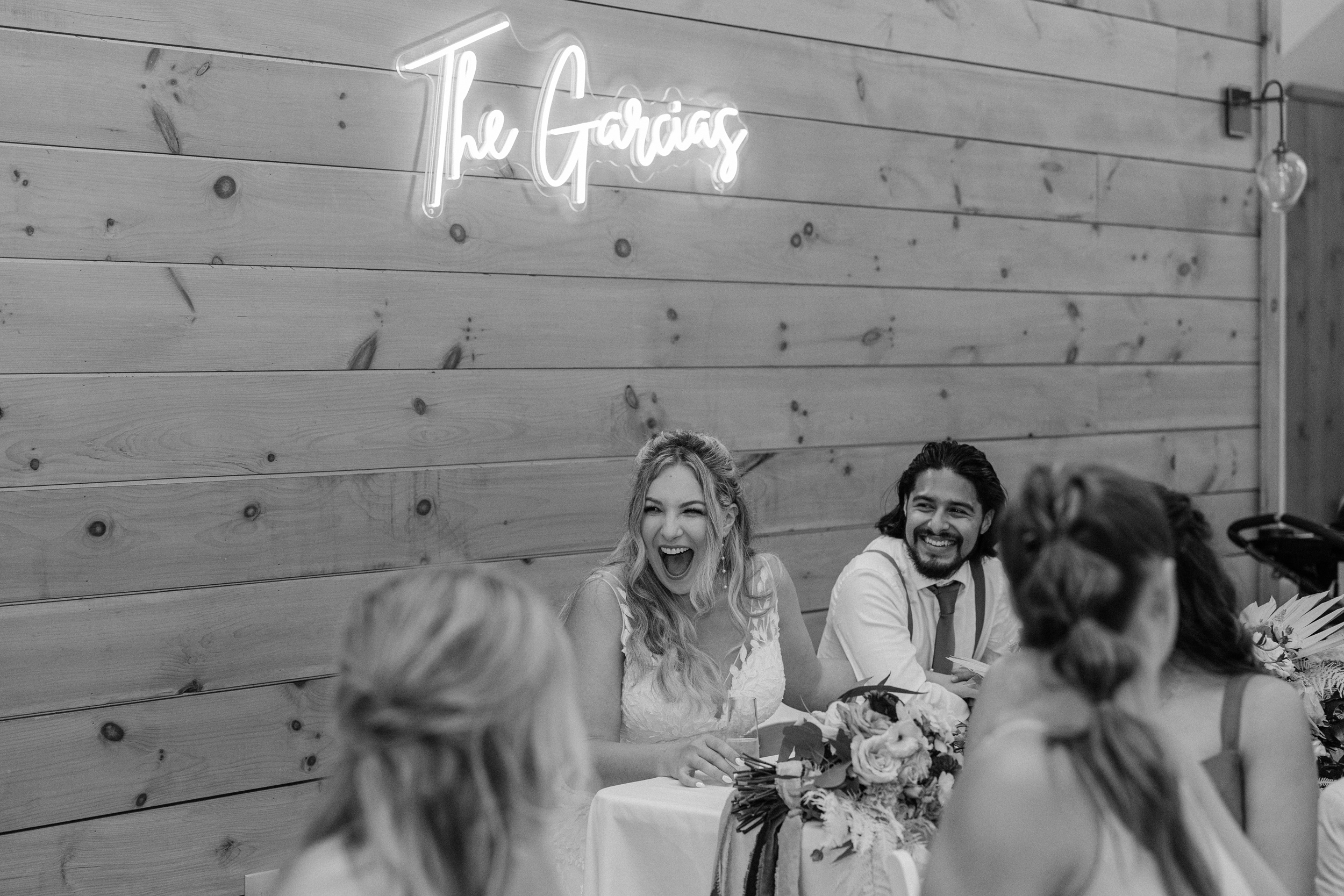 A bride laughs big while sitting at her head table with her laughing groom