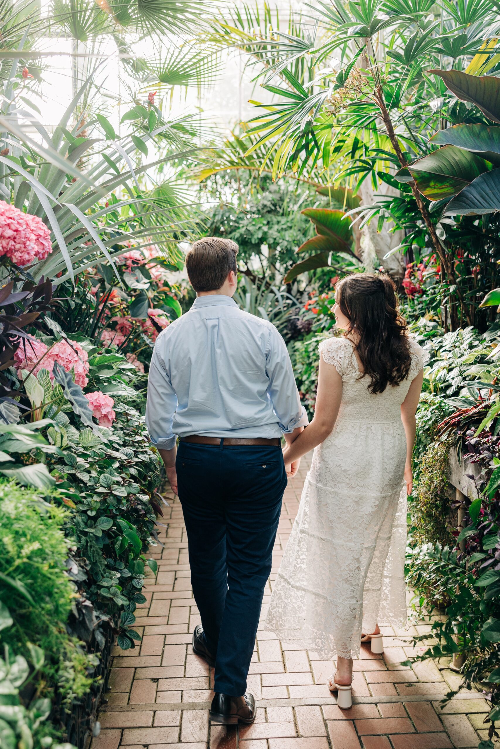 Newlyweds smile at each other while holding hands and walking through the biltmore estate wedding venue greenhouse garden