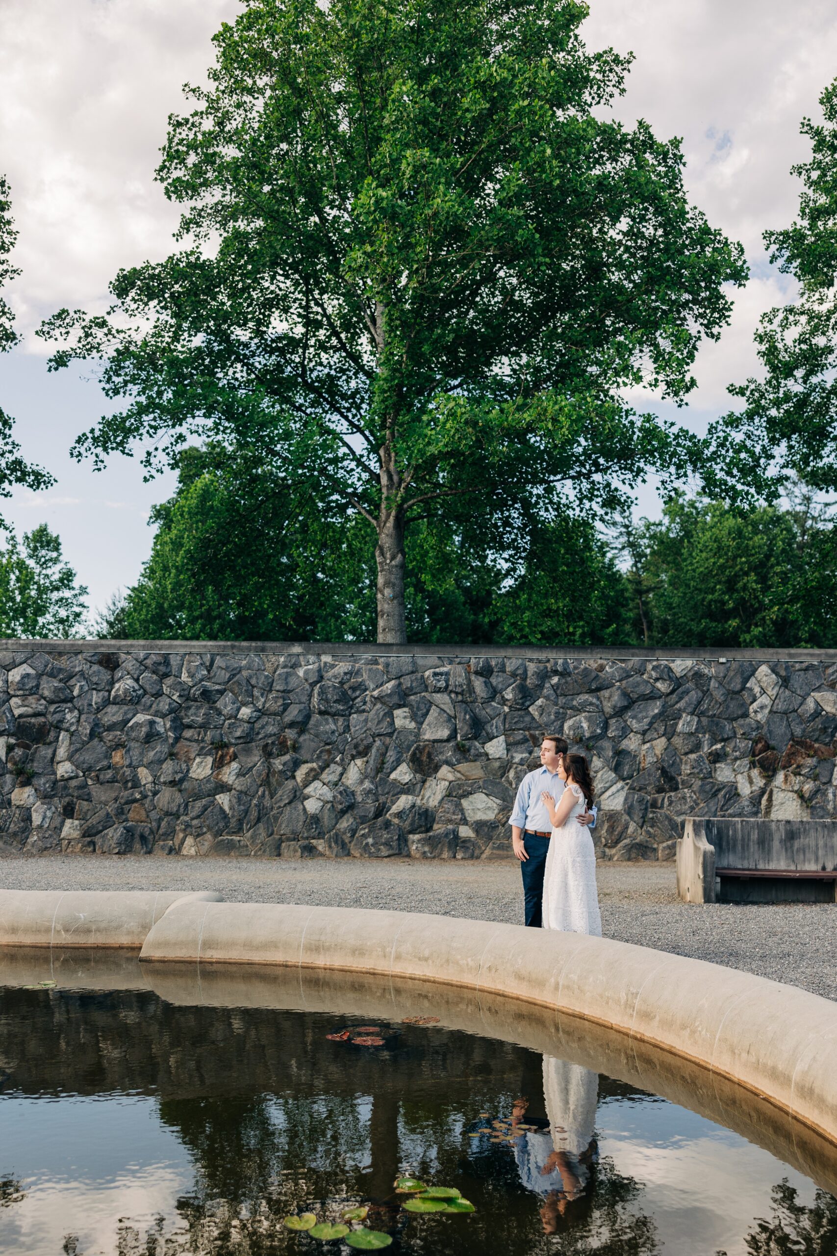 Newlyweds snuggle on the edge of a garden pond at sunset