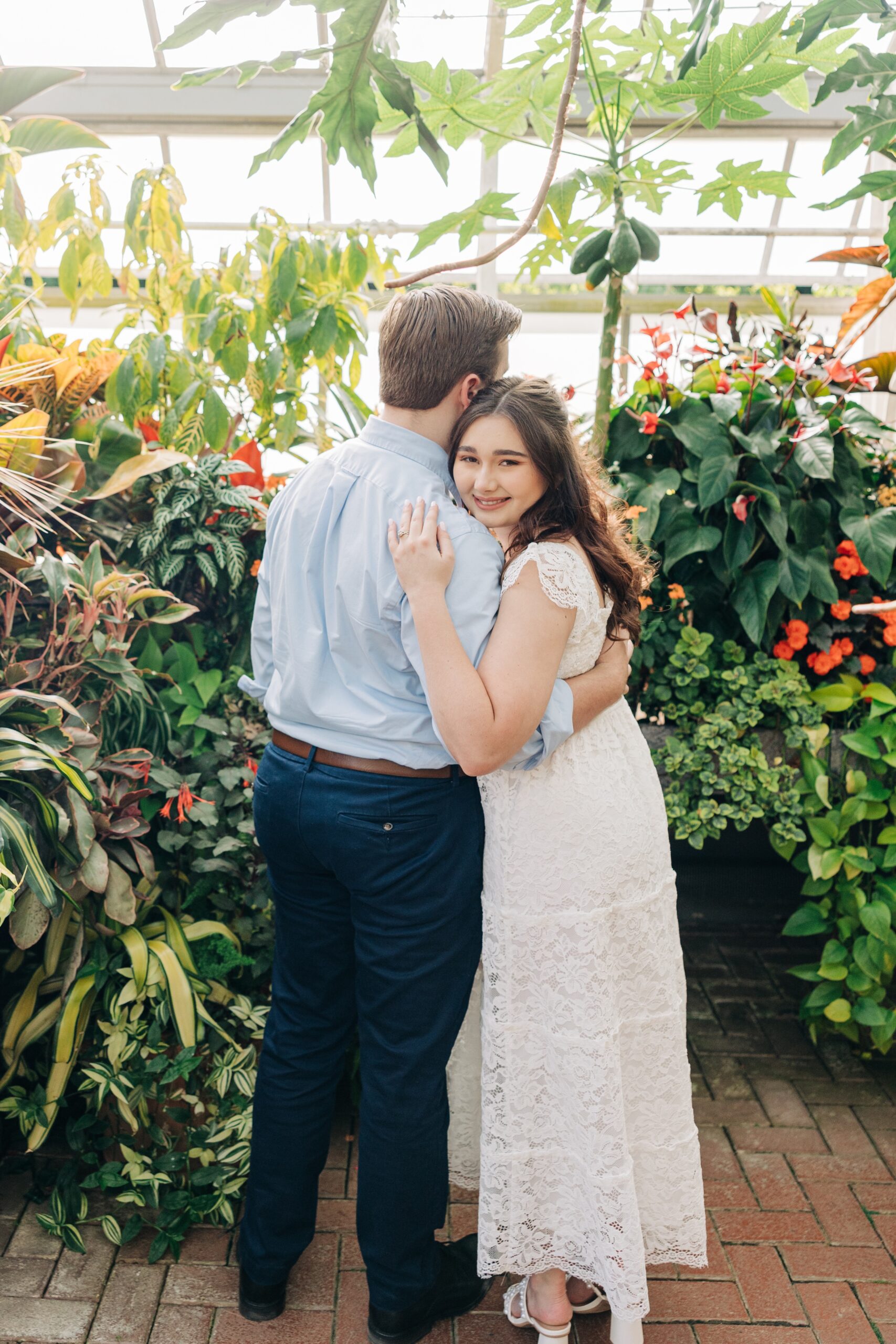 A bride and groom hug while the bride smiles in a greenhouse