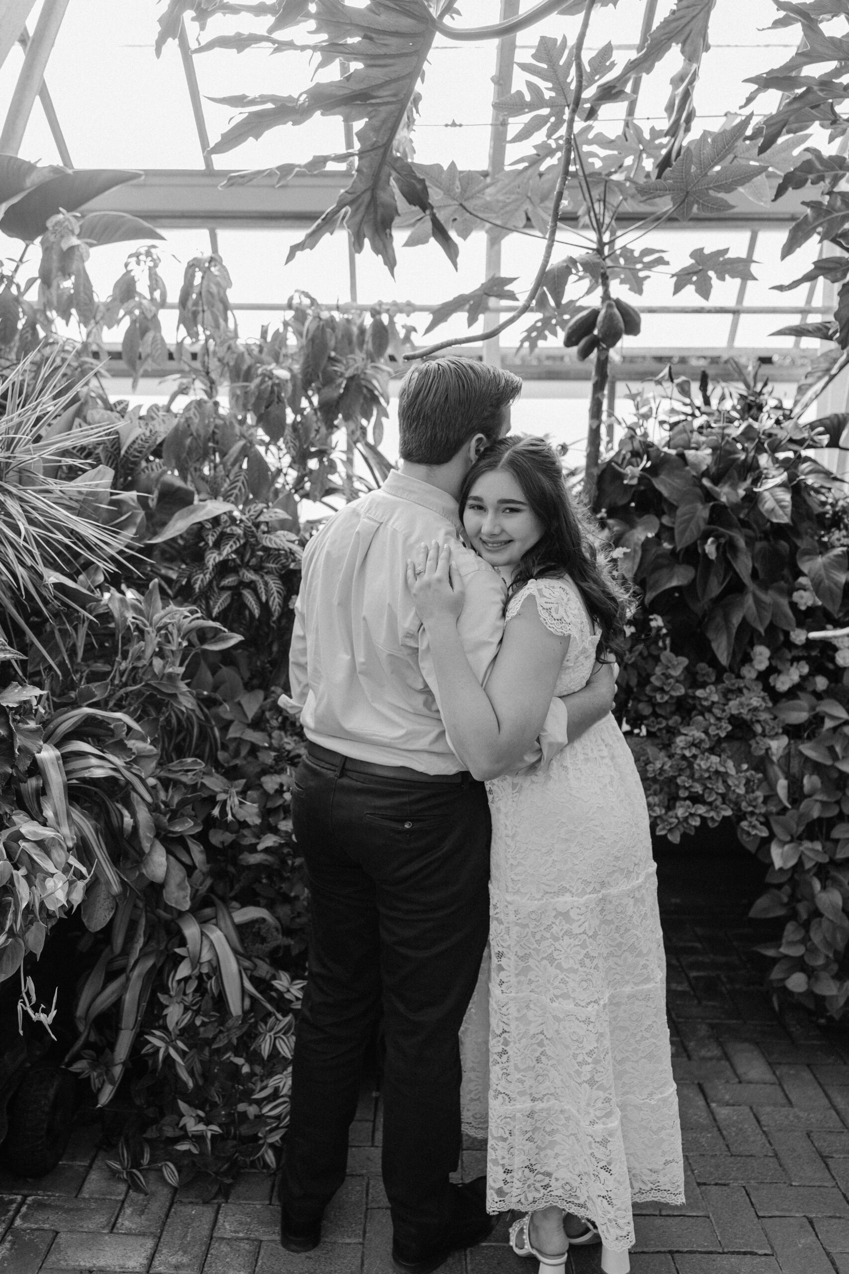 A bride smiles while snuggling on the shoulder of her groom in a greenhouse garden