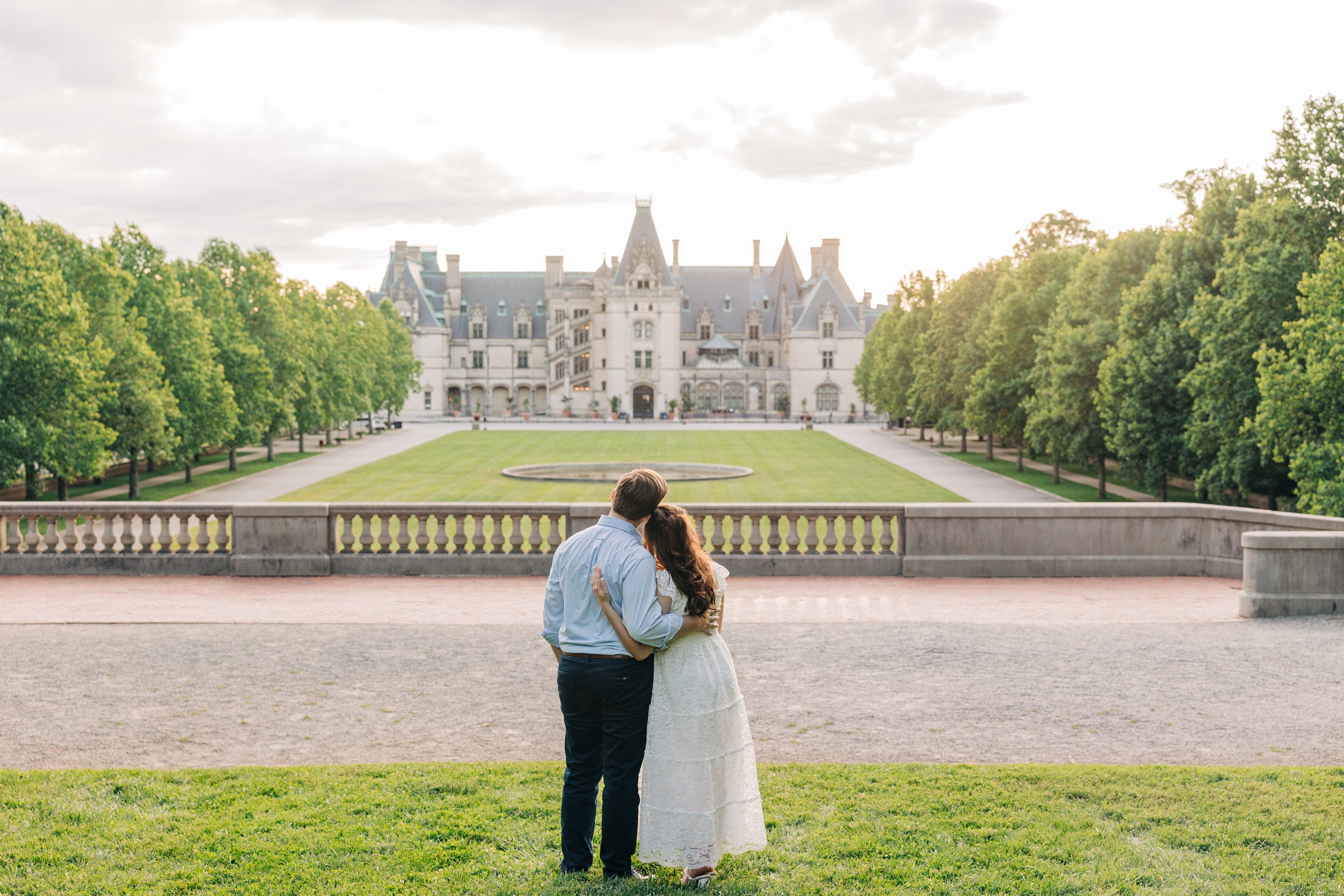 Newlyweds snuggle while standing and gazing back at the biltmore estate wedding venue at sunset