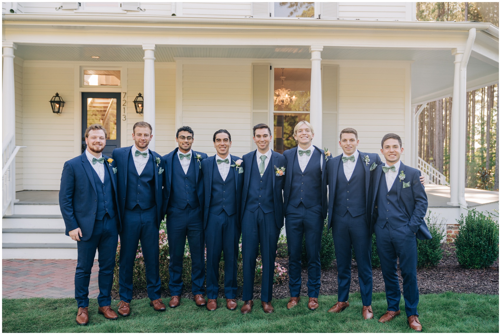 A groom stands outside in the lawn with his groomsmen all in blue suits