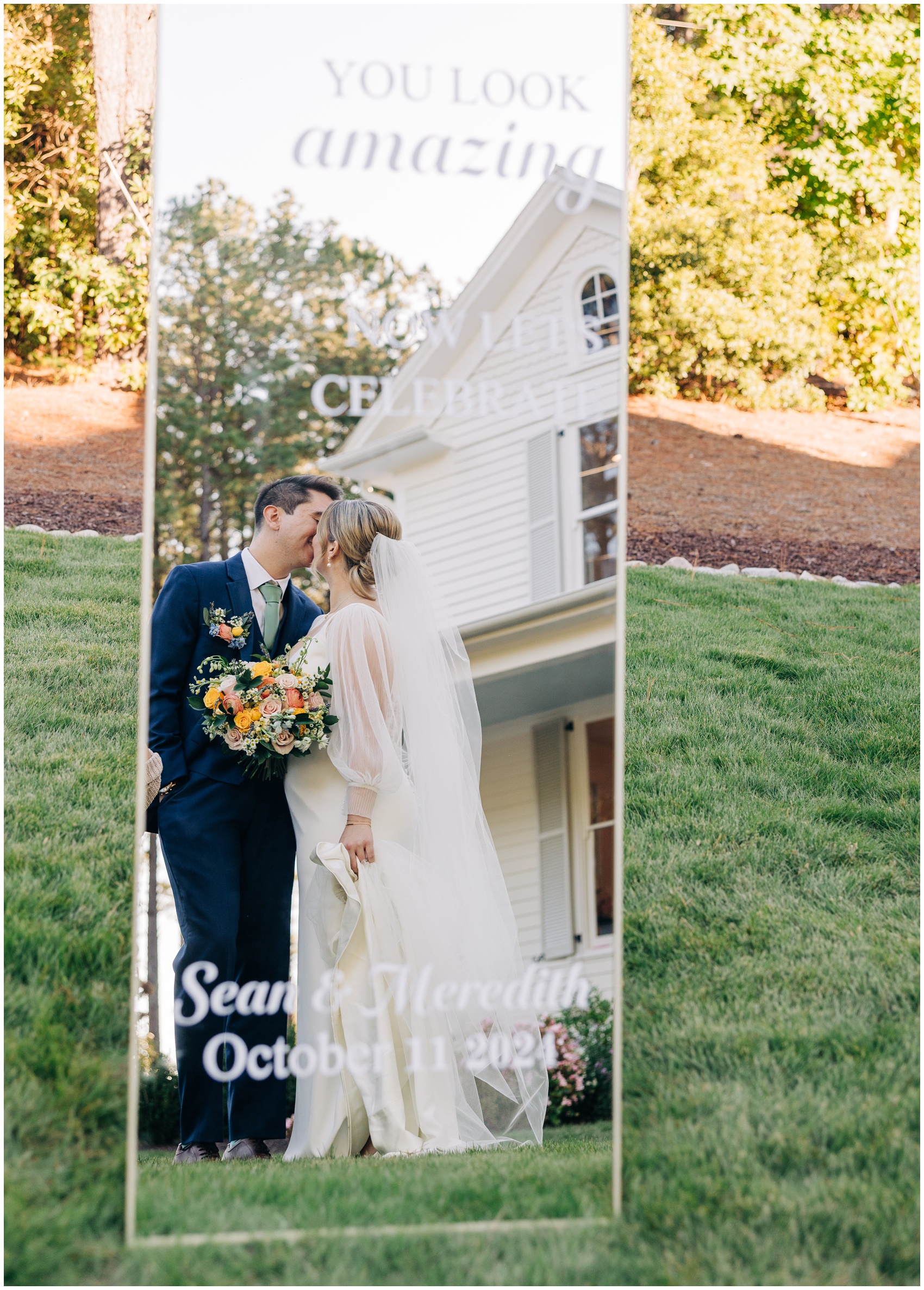 Newlyweds kiss in the lawn in a mirror wedding sign