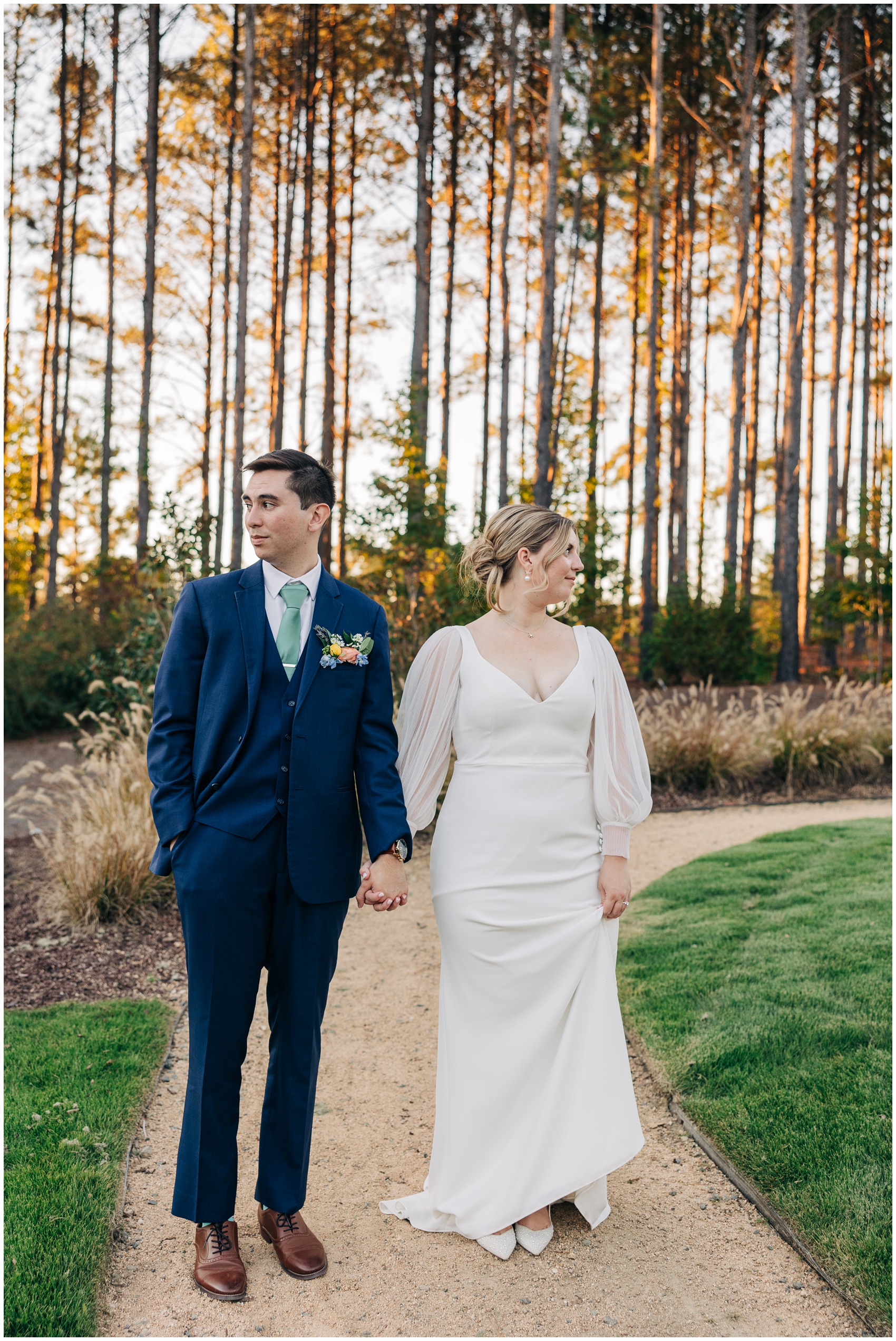 Newlyweds hold hands while walking down a garden path at sunset and looking around the upchurch wedding venue