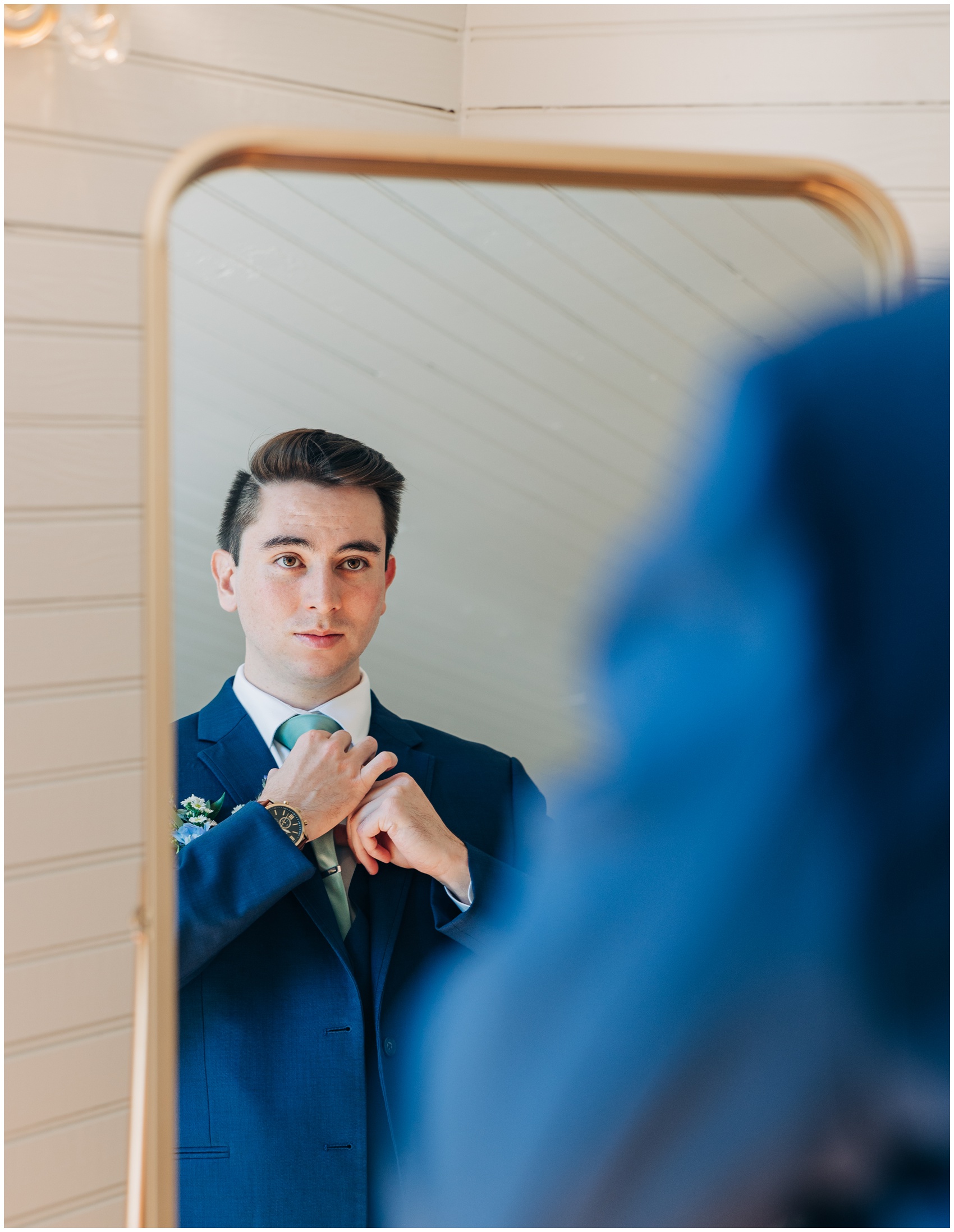 A groom adjusts his tie while getting ready in a mirror