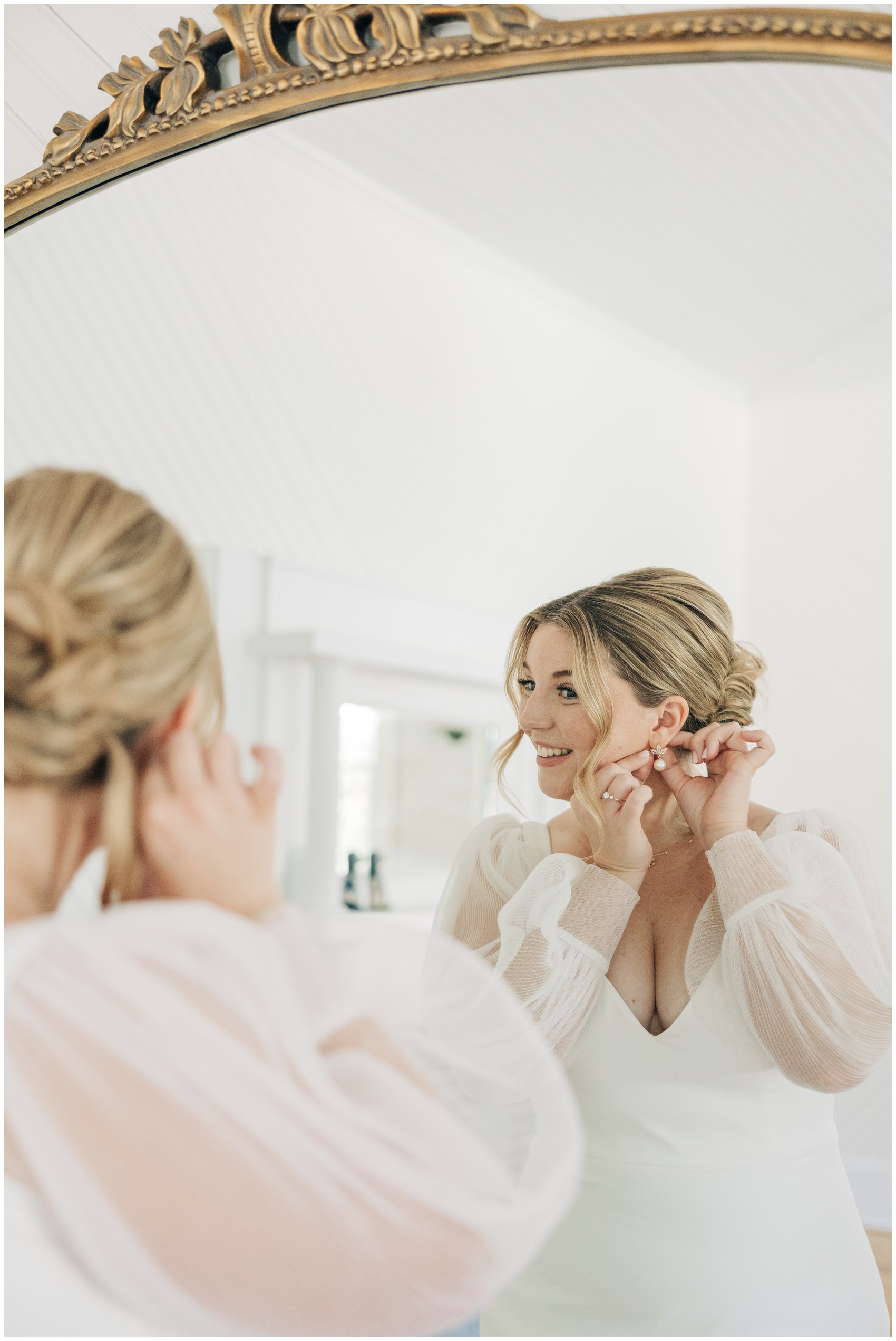 A bride puts on her pearl earrings in a large ornate mirror