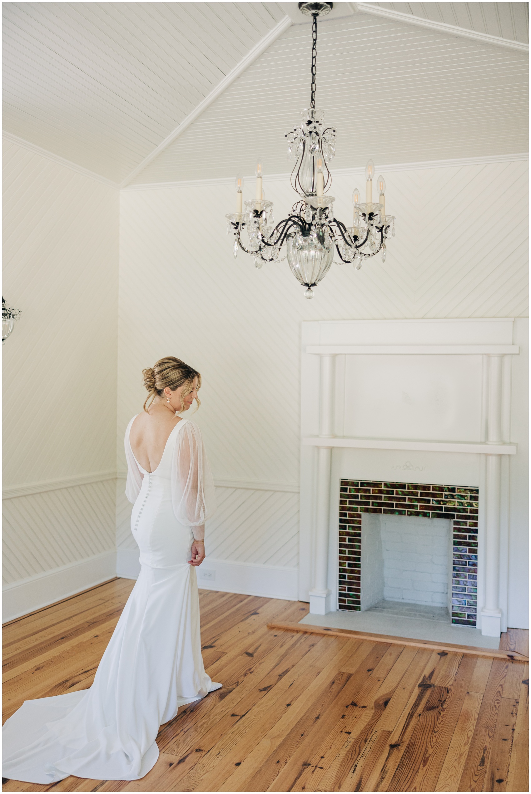 A bride walks by the fireplace under a chandelier in her dress