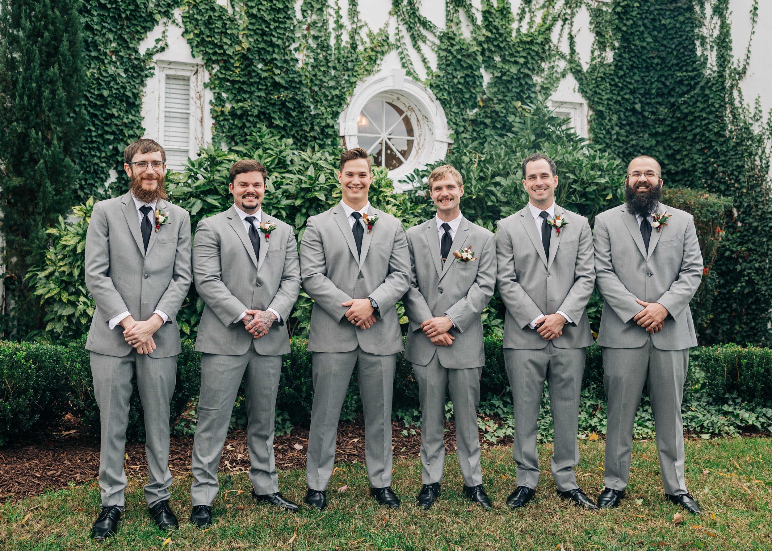 A groom smiles while standing with his groomsmen in matching grey suits