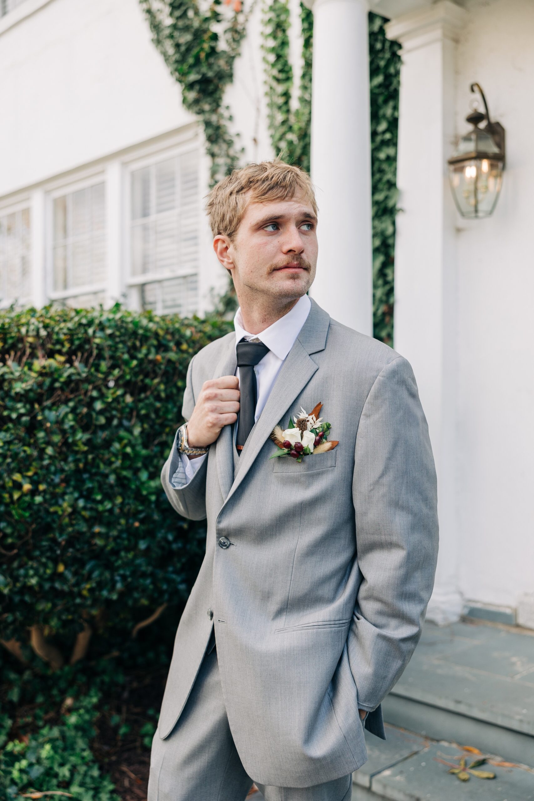 A groom holds his grey suit lapel while looking back over his shoulder