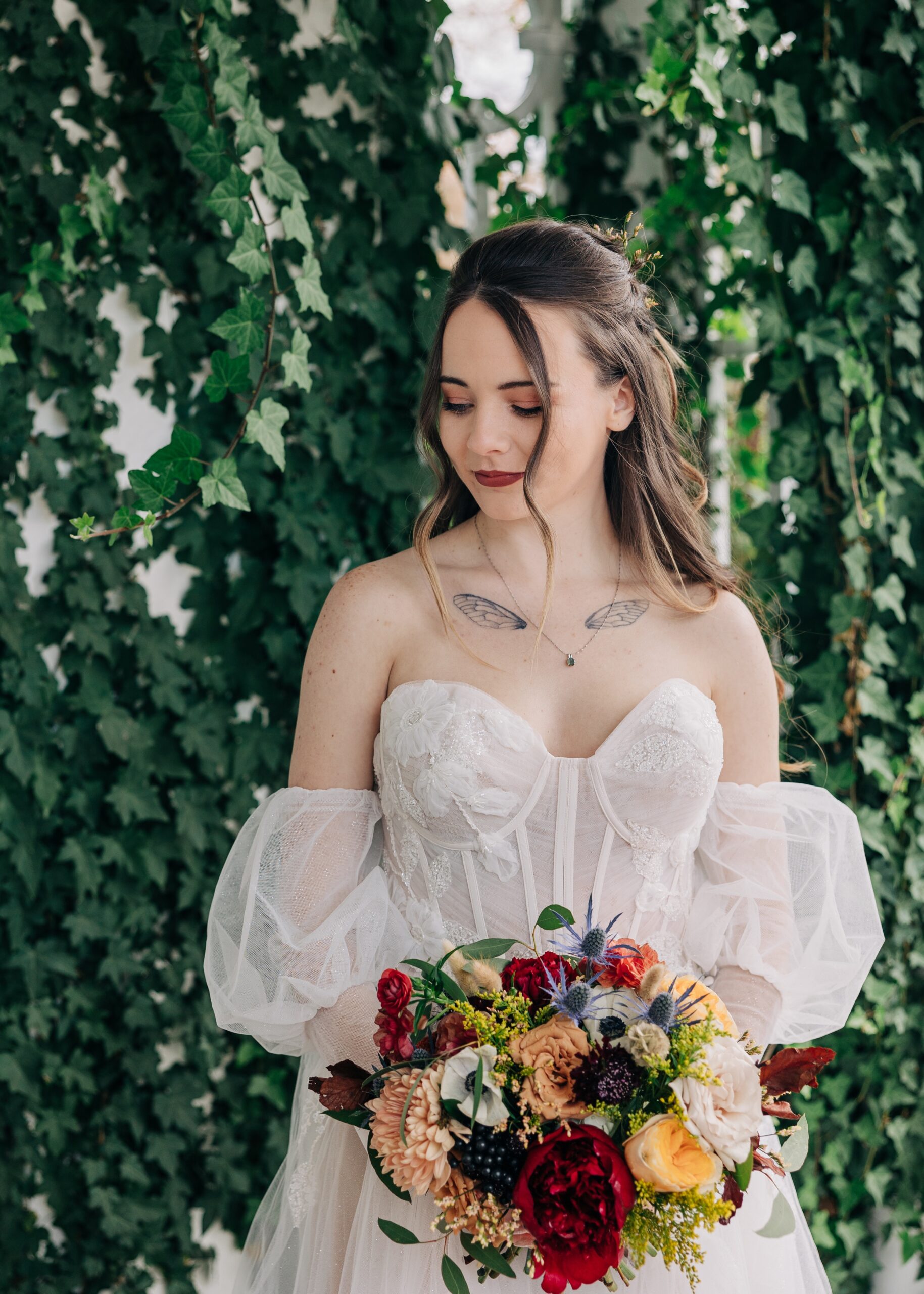 A bride stands holding her colorful bouquet and smiling down her shoulder