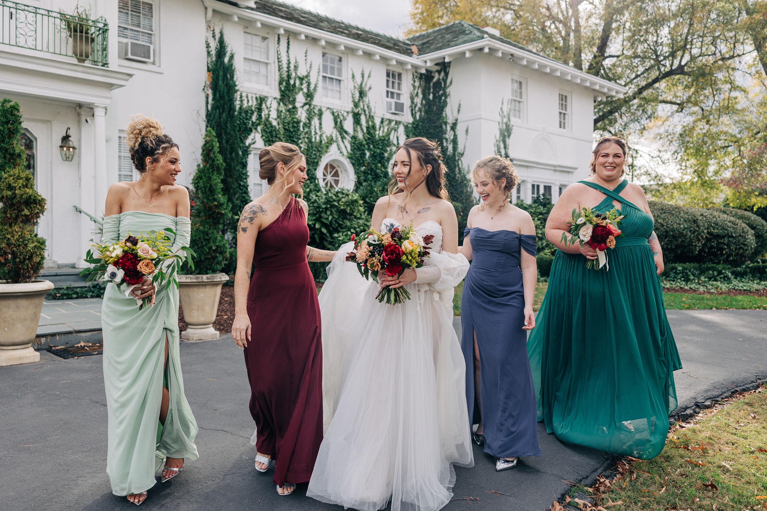 A bride laughs while walking with her bridesmaids in different color dresses at The Finch House