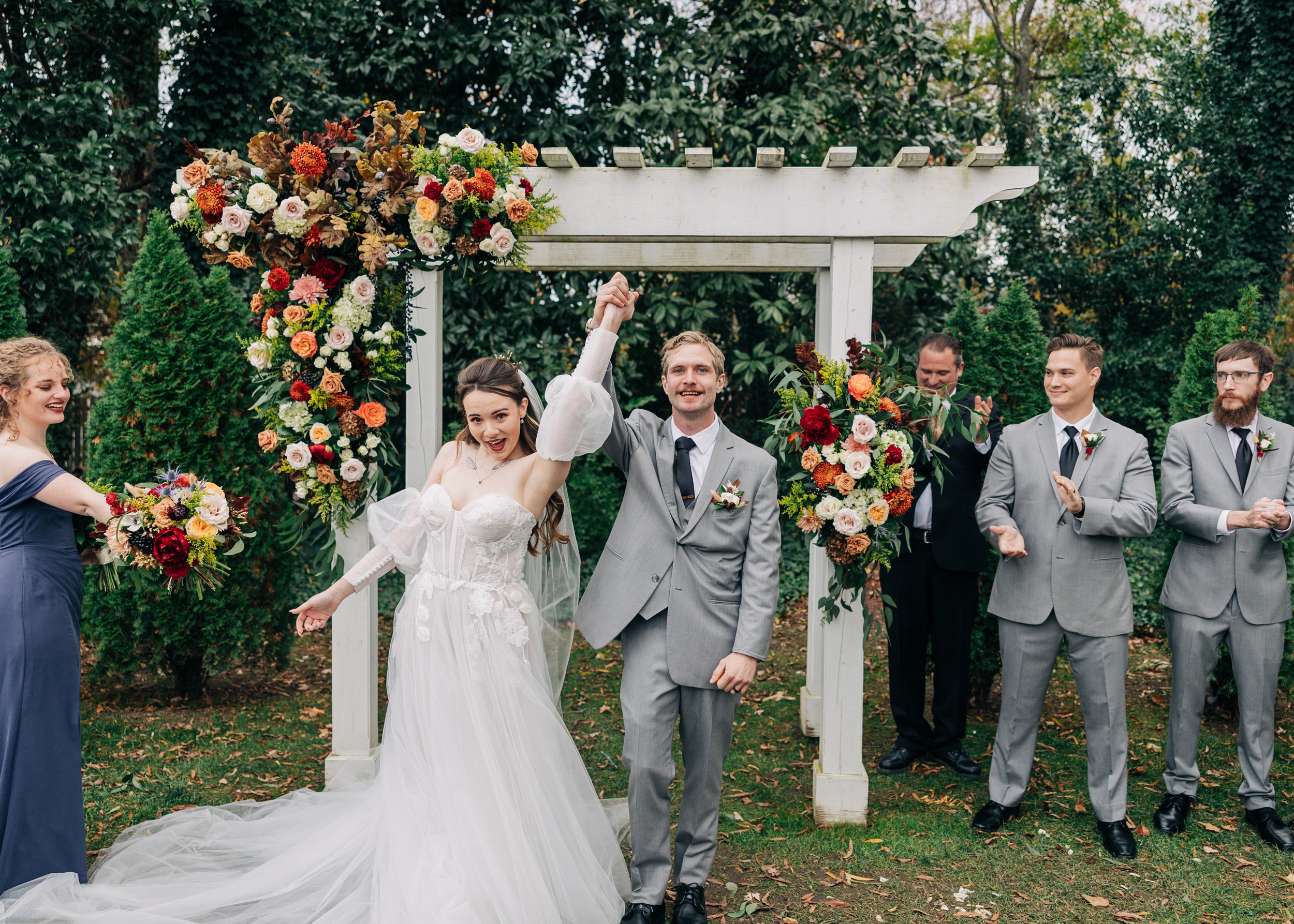 Newlyweds lift their hands and celebrate to end their ceremony under a white arbor at The Finch House