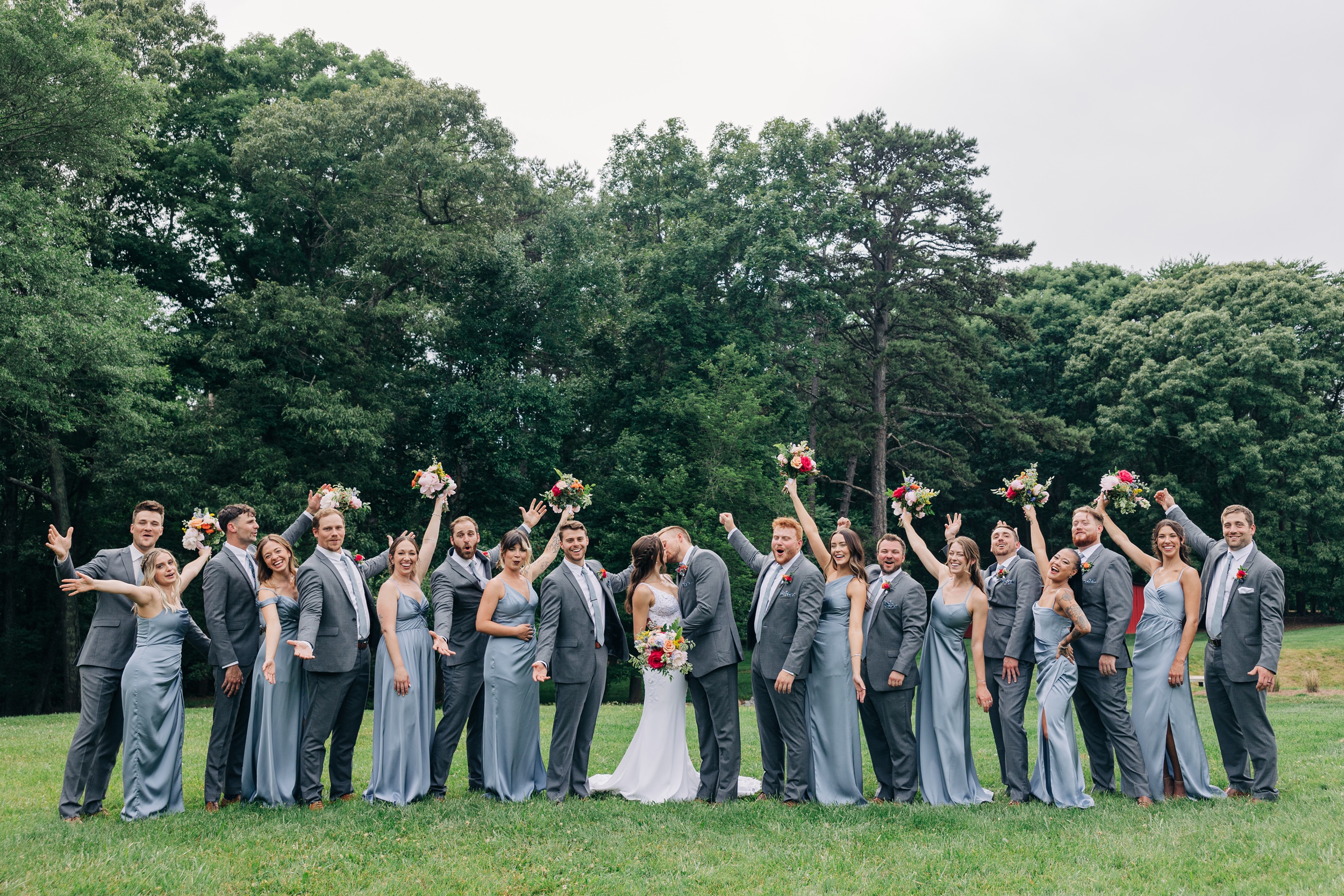 Newlyweds kiss while their bridal party celebrate in the lawn of The Ivory Barn