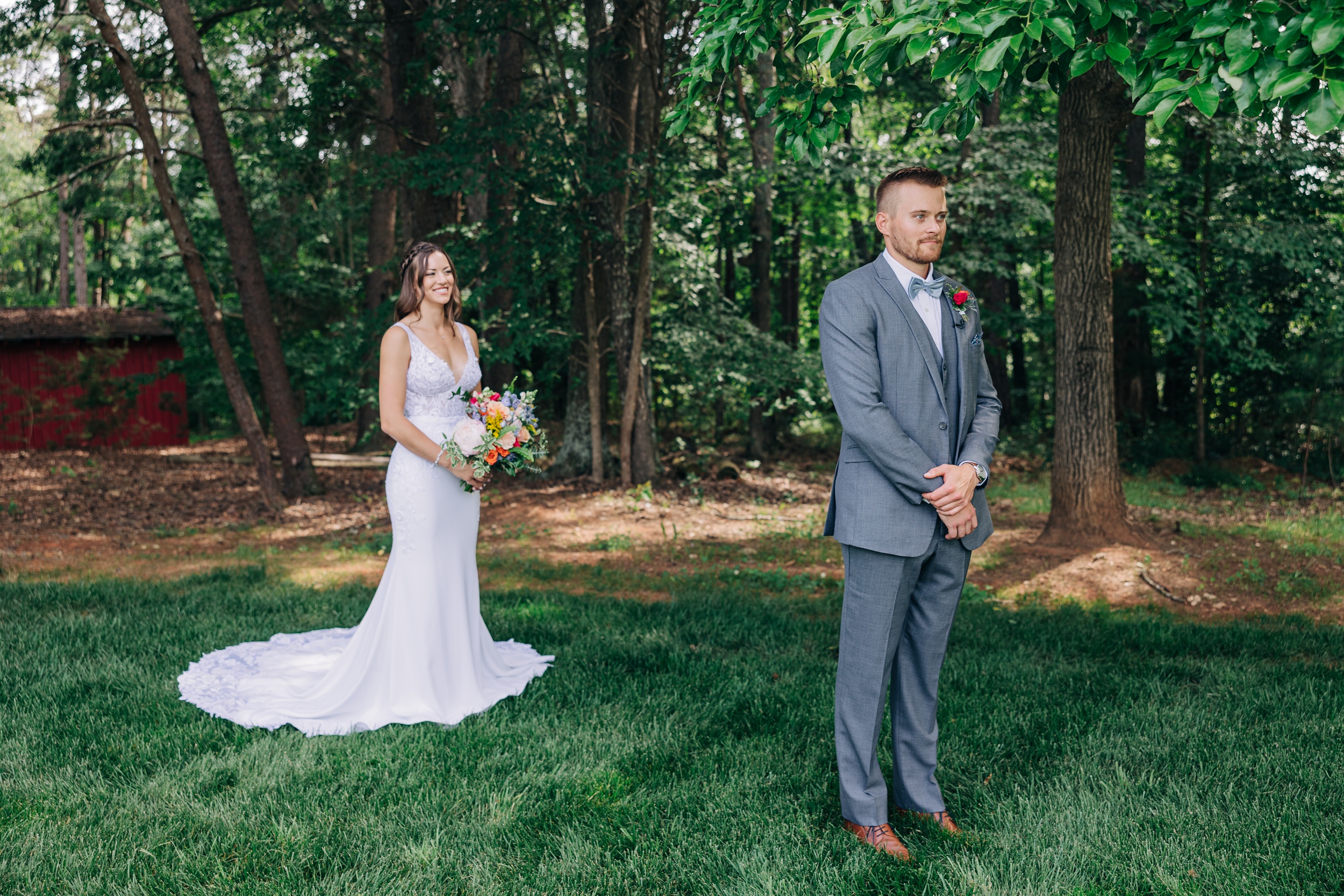 A groom nervously waits for his bride behind him for their first look in the lawn of The Ivory Barn