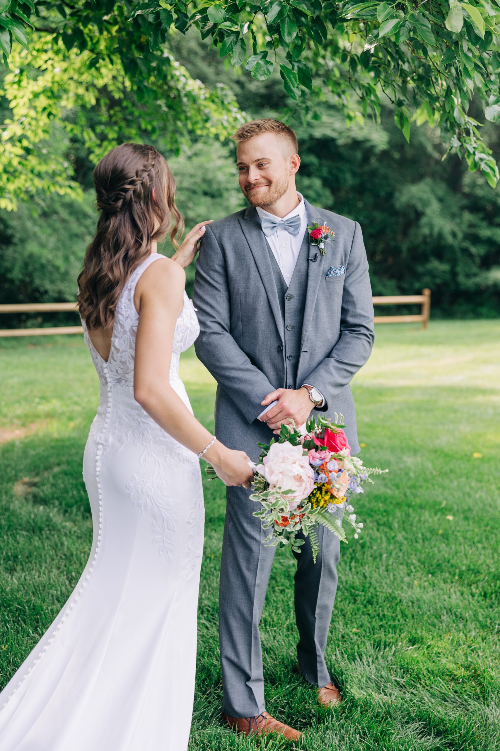 A groom smiles as he sees his bride for the first look under a tree