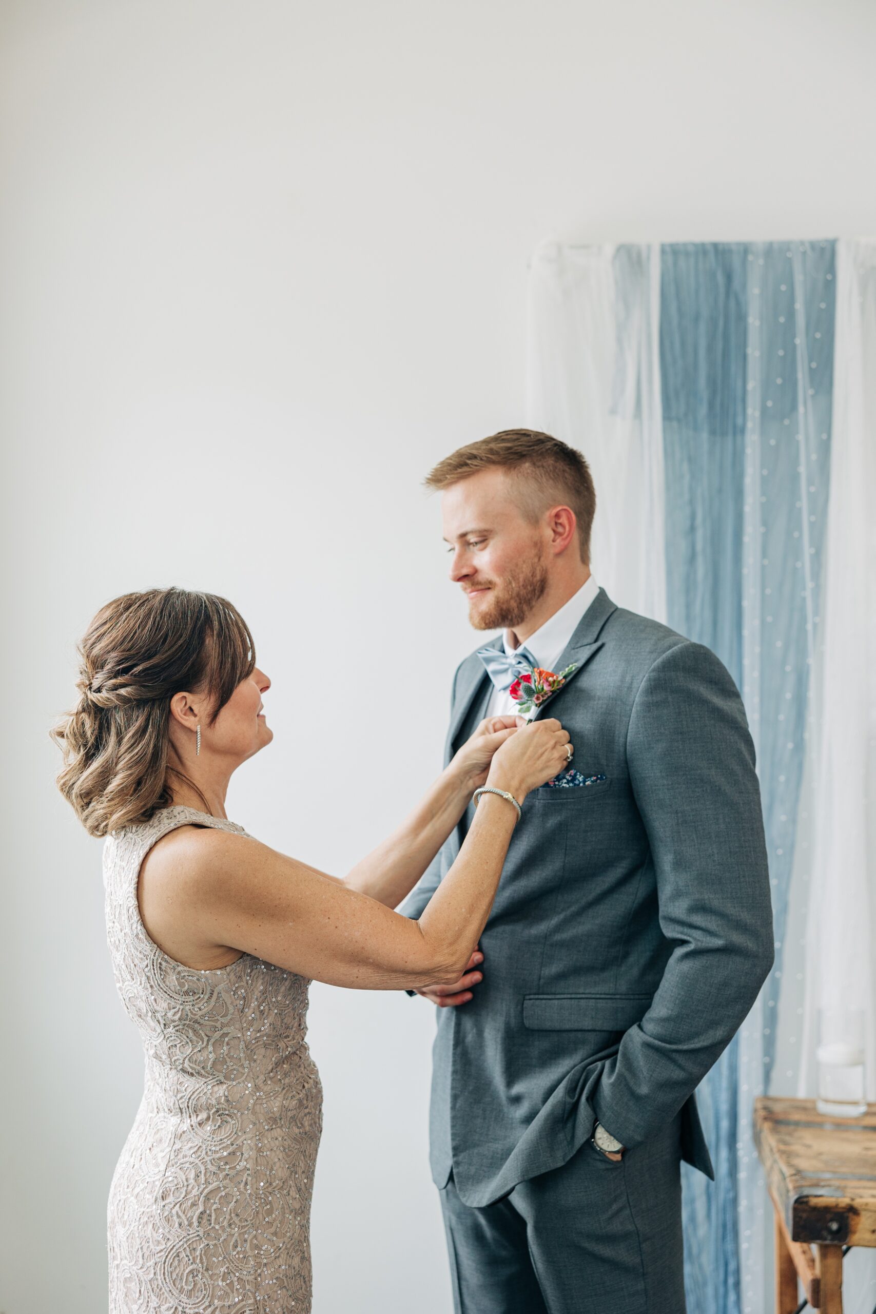 Mom in a gold dress helps her son fix his boutonniere before his wedding