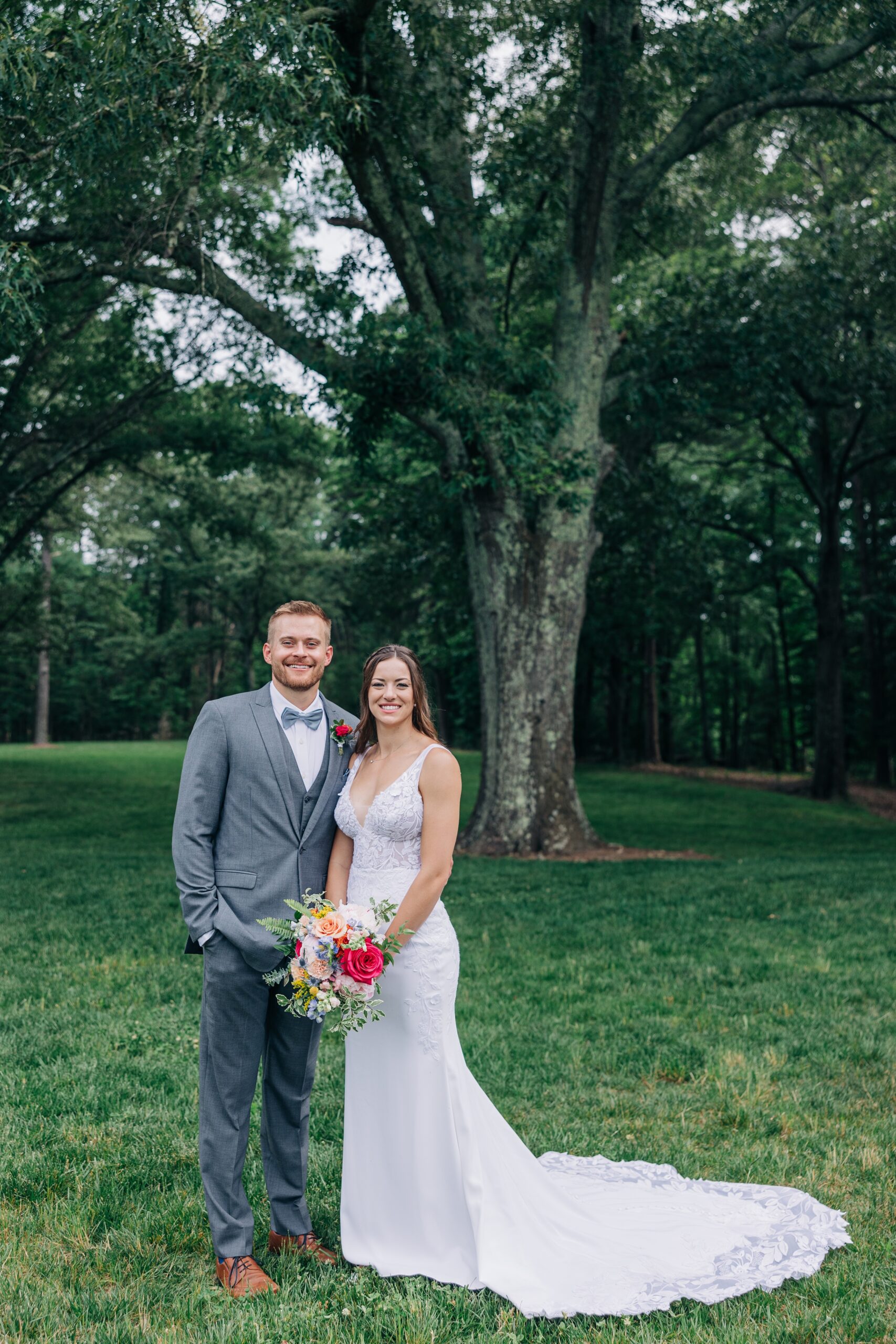 Newlyweds smile together while standing under a large oak tree