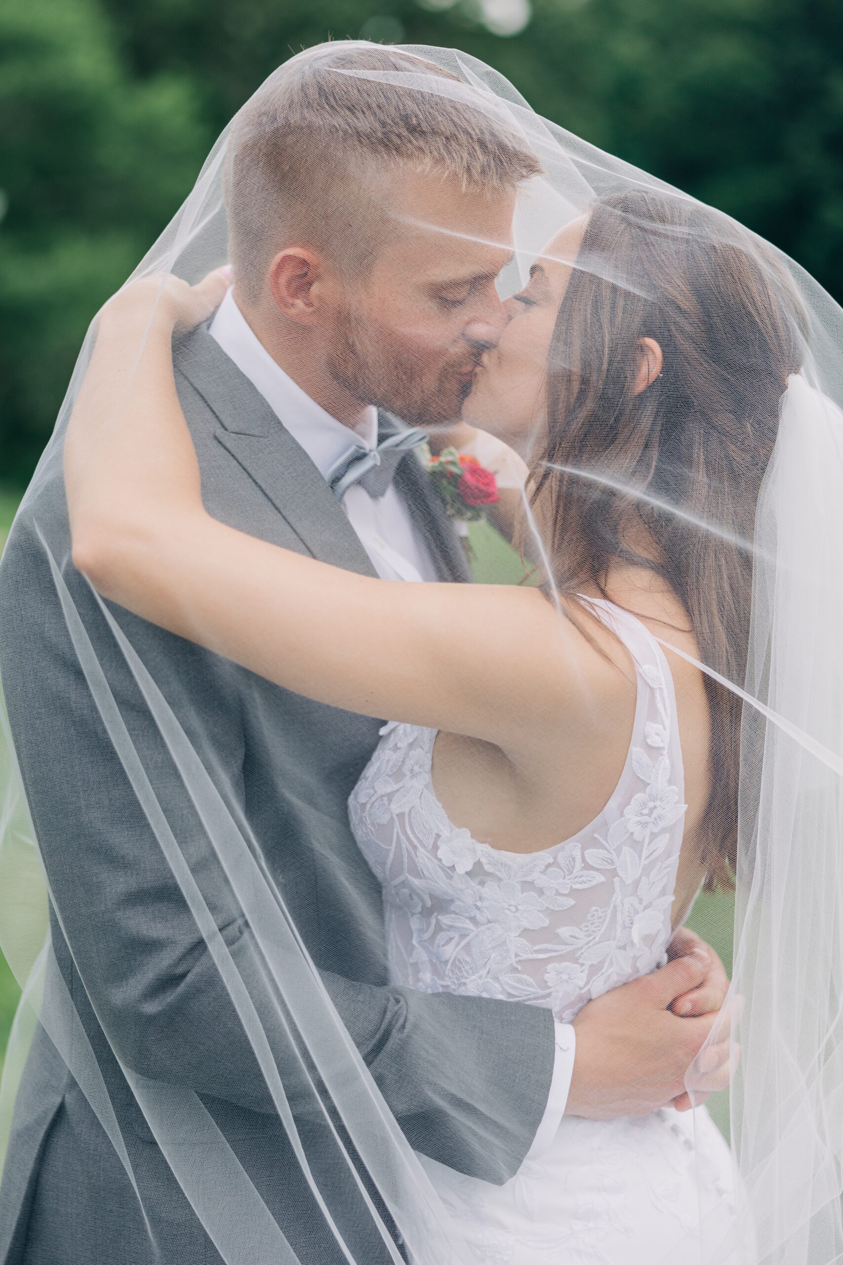 Newlyweds kiss under the veil in a grassy lawn