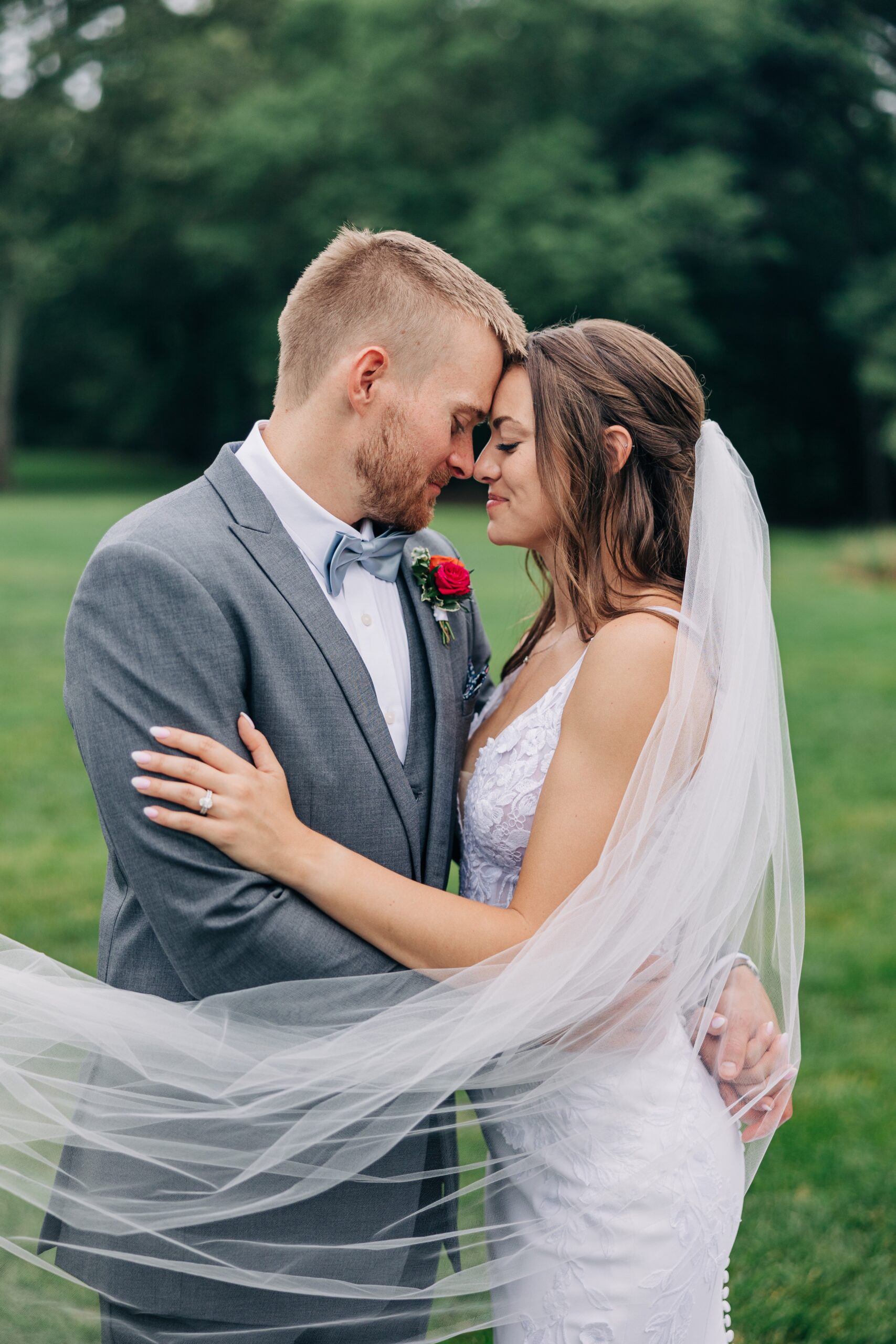 A bride and groom snuggle in the lawn while wrapped in the veil at The Ivory Barn wedding venue