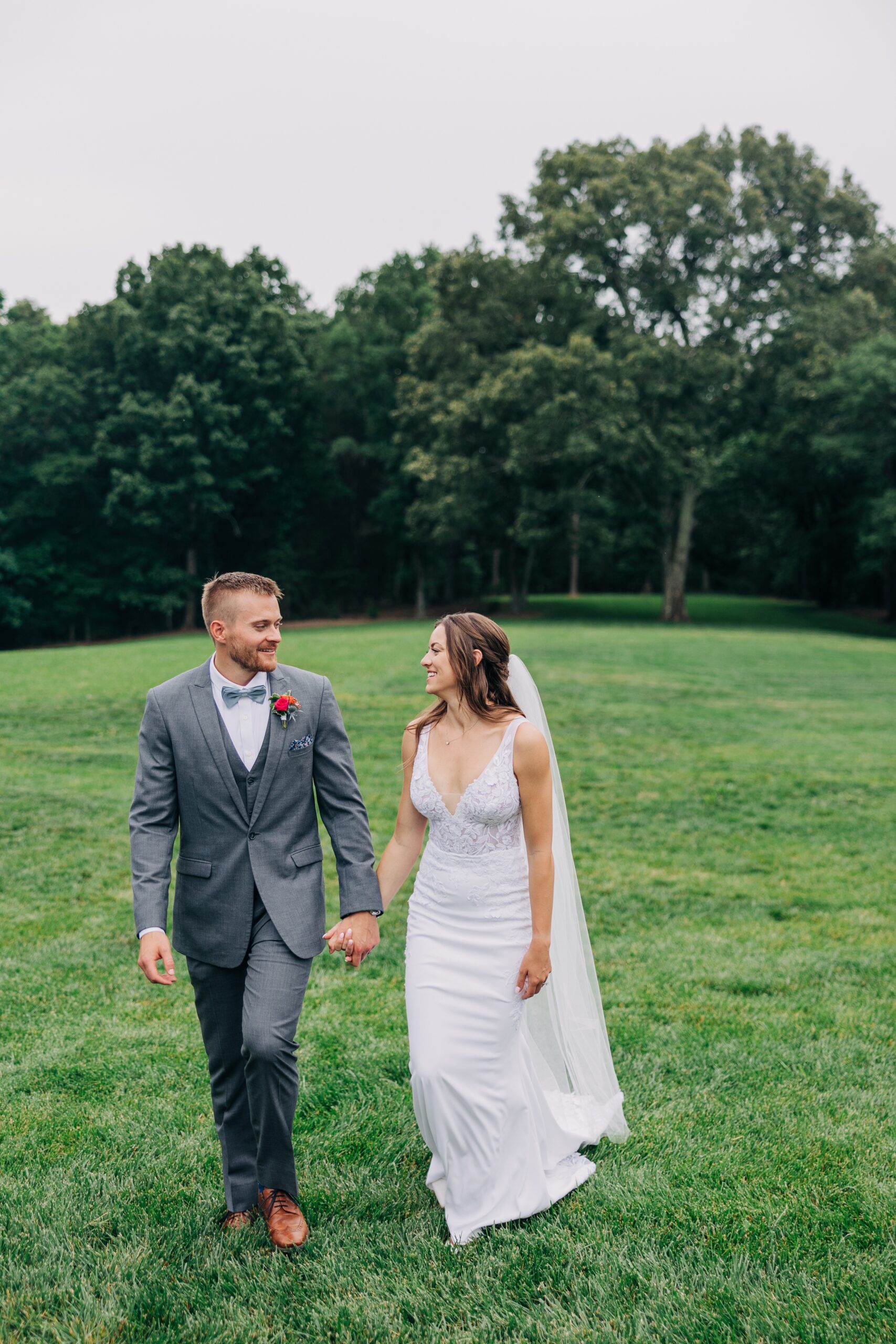 A happy newlywed couple holds hands and smiles at each other while walking in the lawn at The Ivory Barn