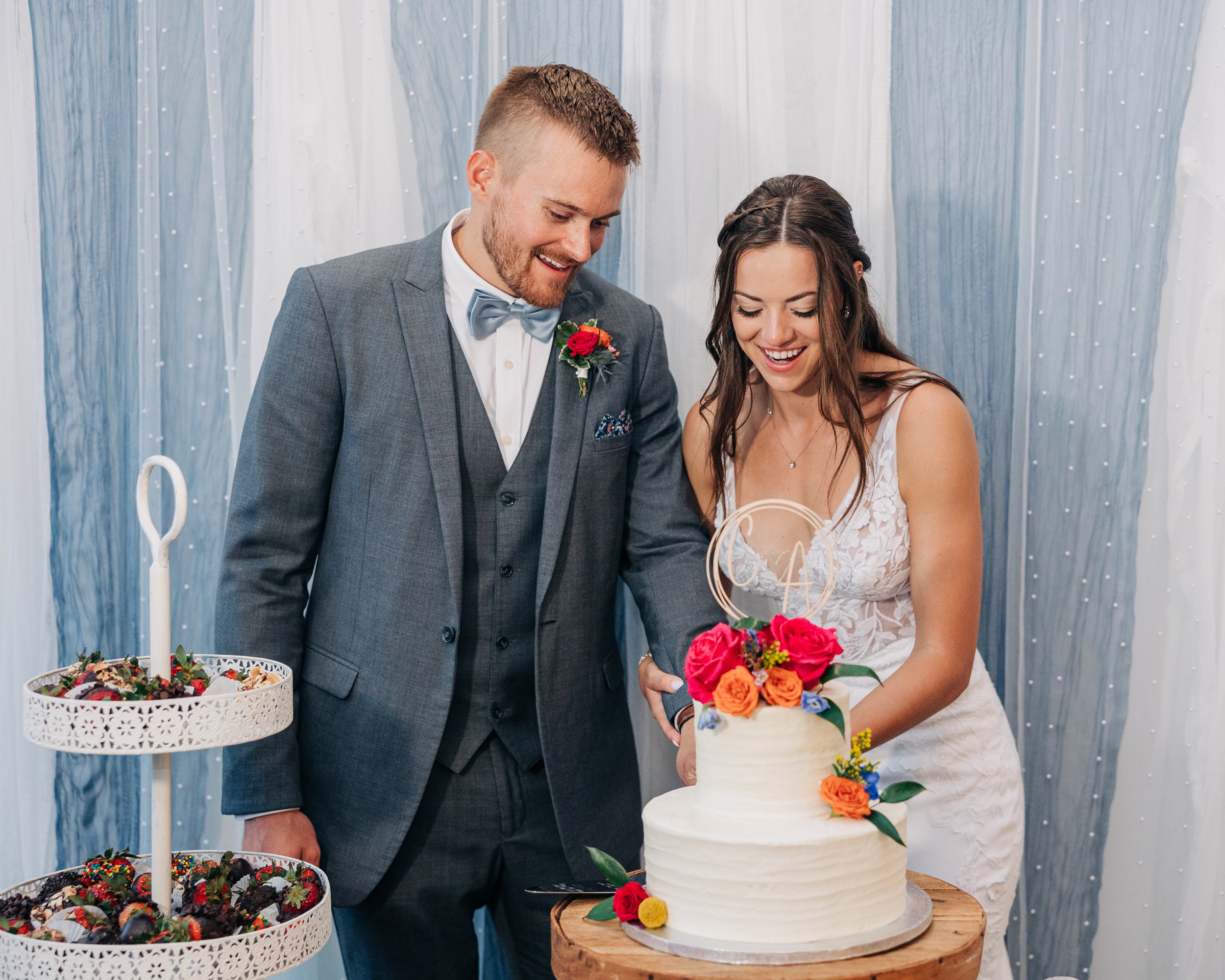 A bride and groom happily cut their two tier cake in front of a linen wall