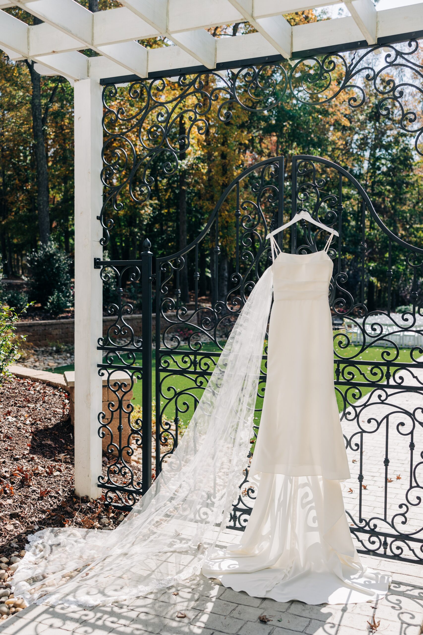 A bride's dress hangs on an iron fence under a pergola