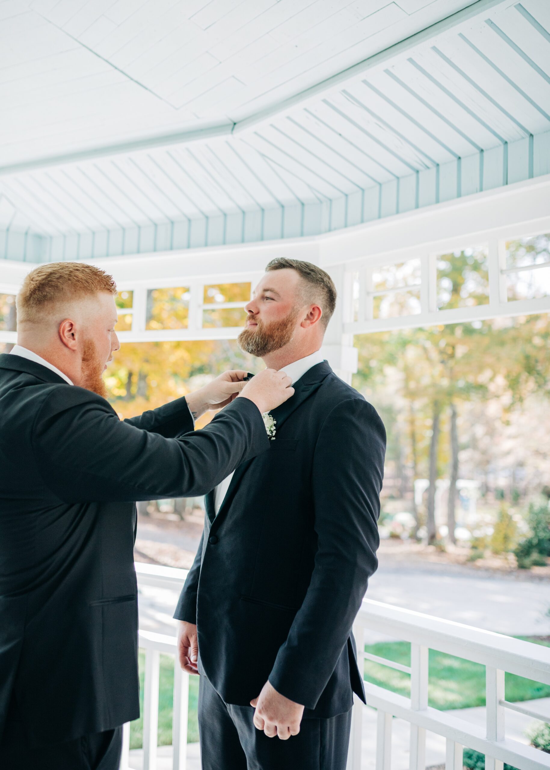 A groomsman helps a groom adjust his bowtie on the covington gardens porch