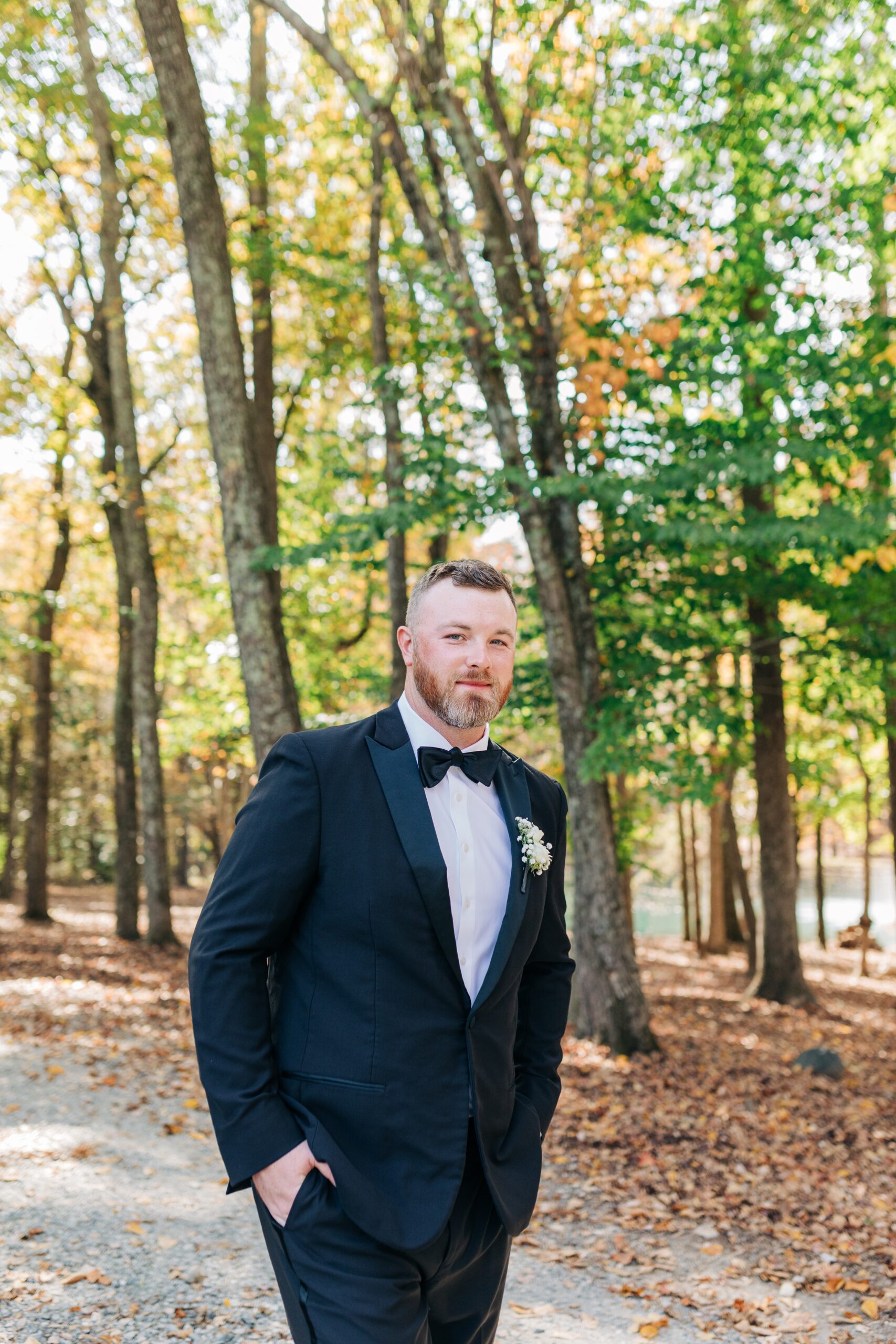 A groom walks in a forest path with hands in pockets in black tux