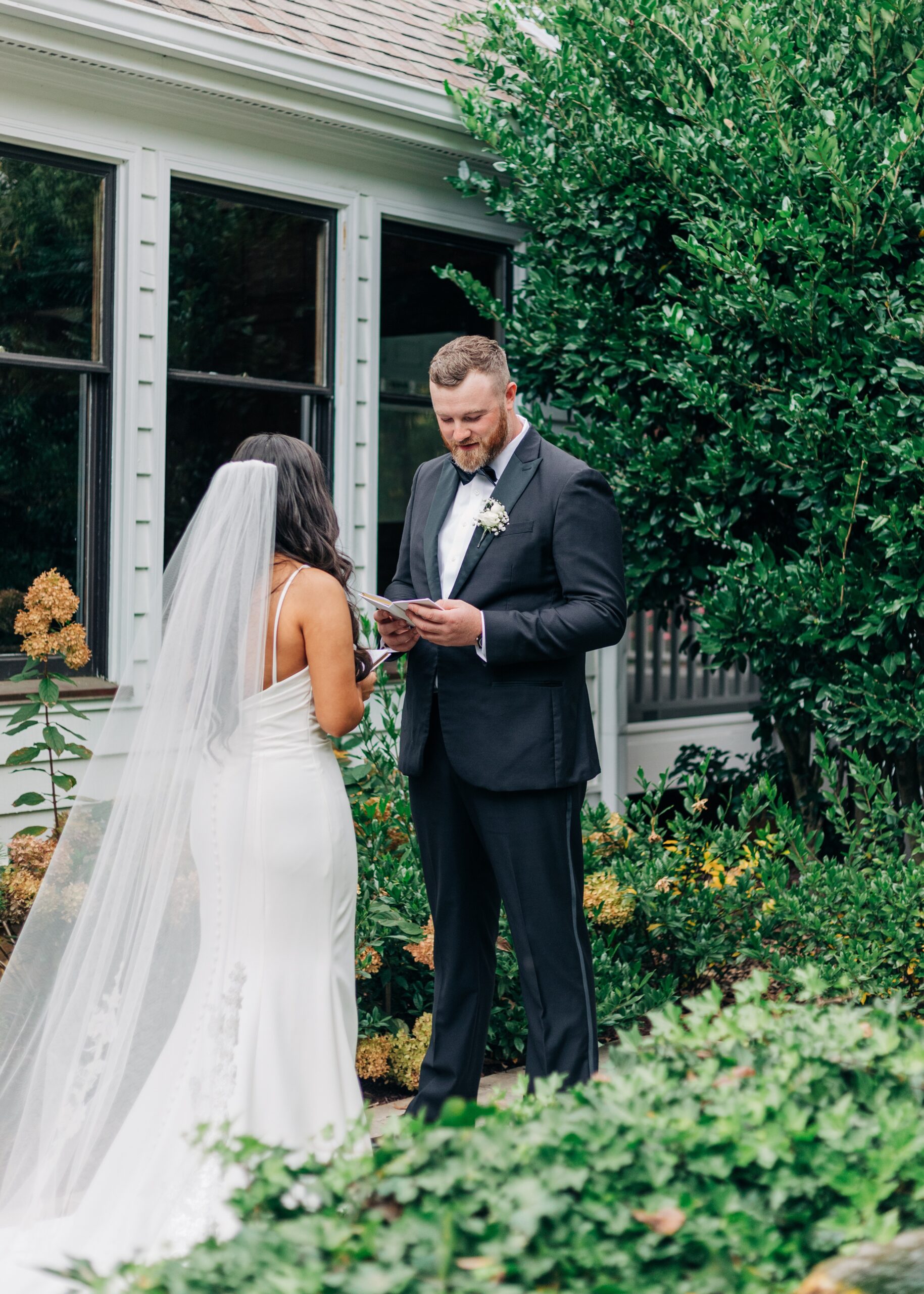 A bride and groom exchange letters in a garden during first look