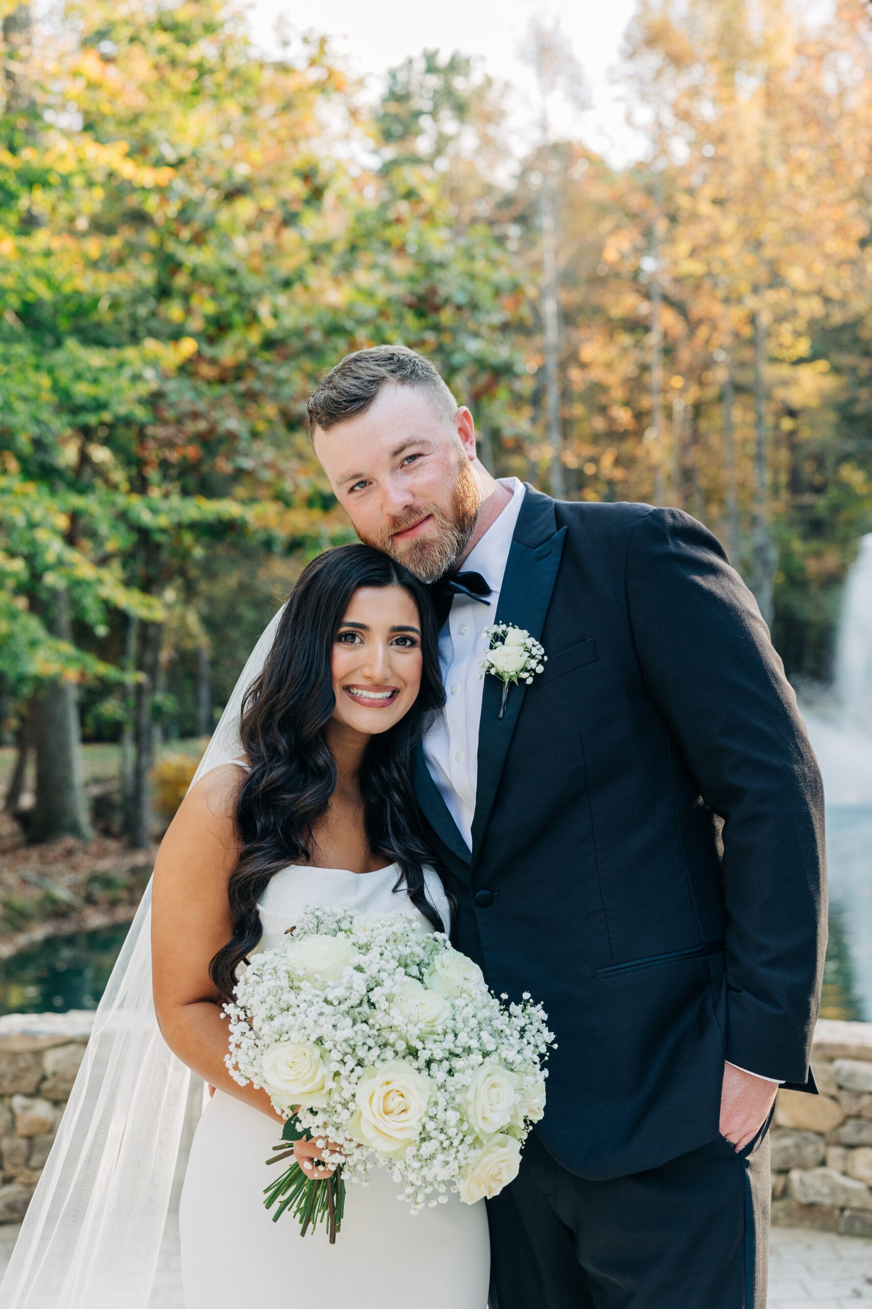 Newlyweds stand by the fountain in the garden smiling and snuggling